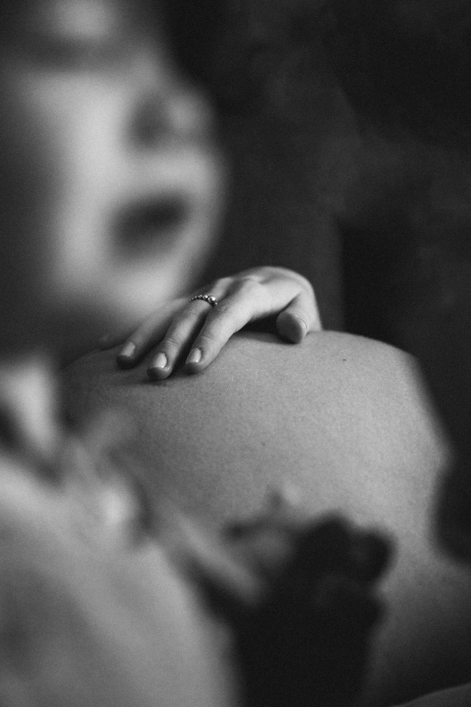 Black and white artistic close-up of a hand with engagement ring resting on bare skin.