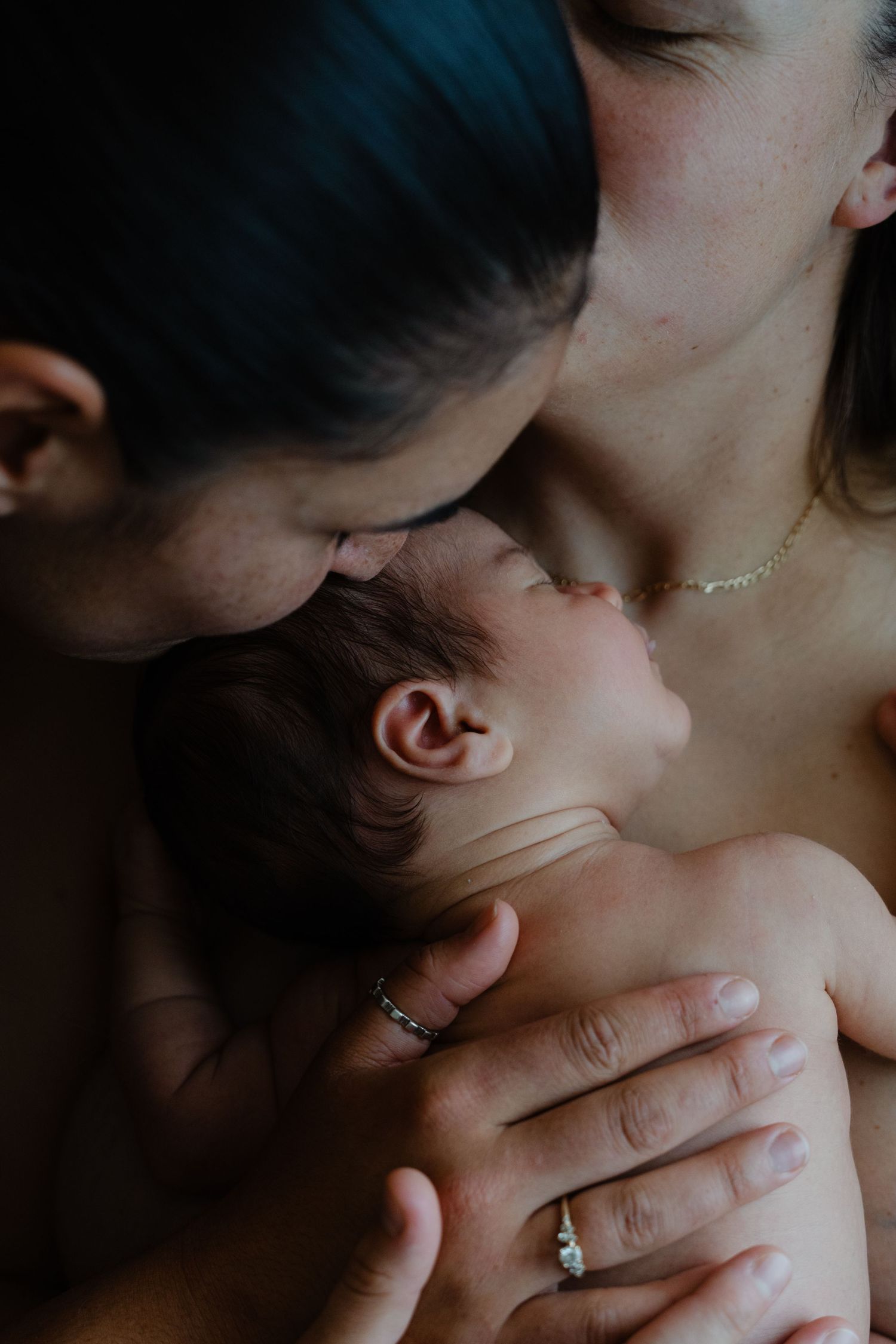Two mothers tenderly holding and kissing their newborn baby, capturing an intimate family bonding moment.