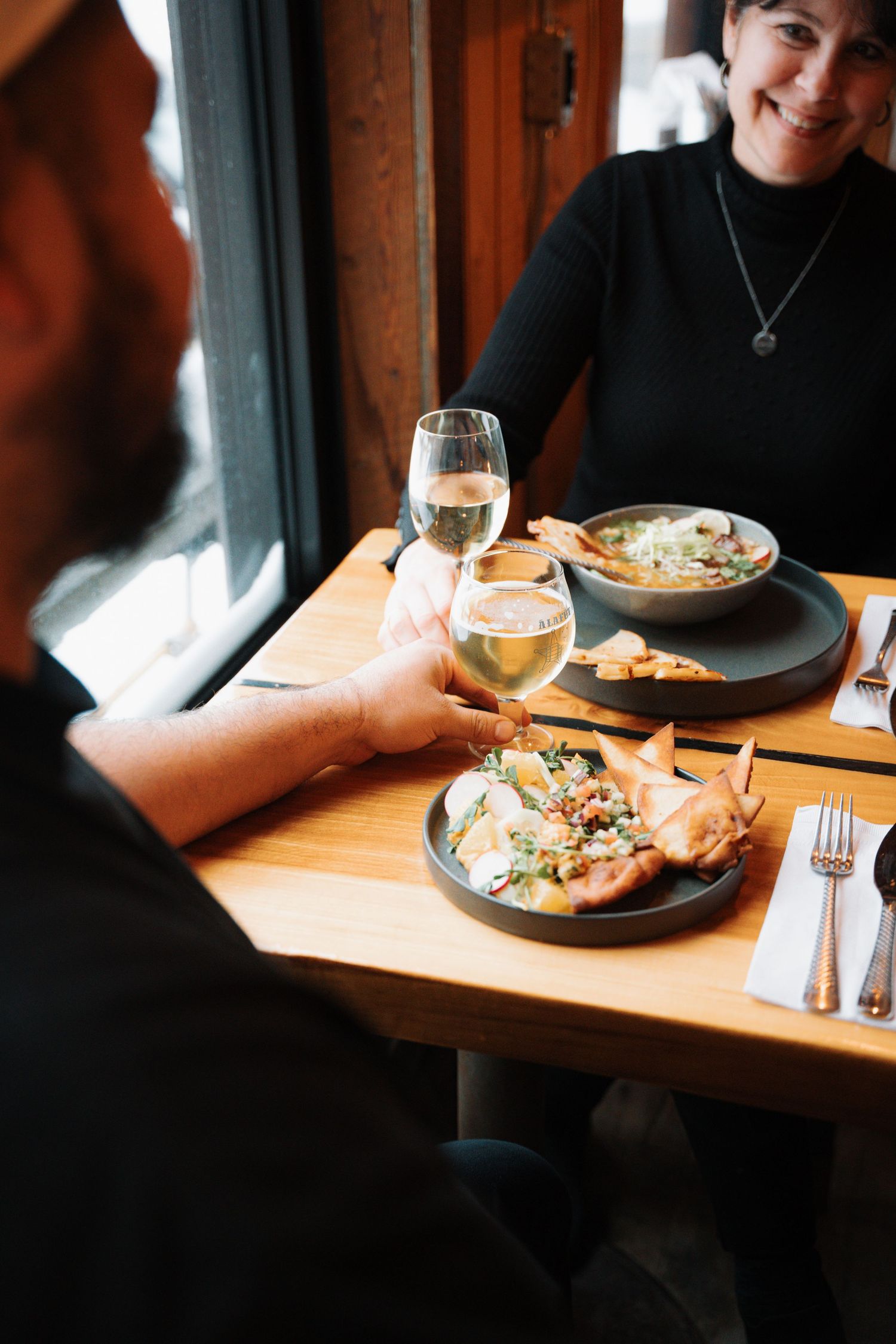 Couple enjoying white wine and gourmet food at a cozy restaurant table by the window.