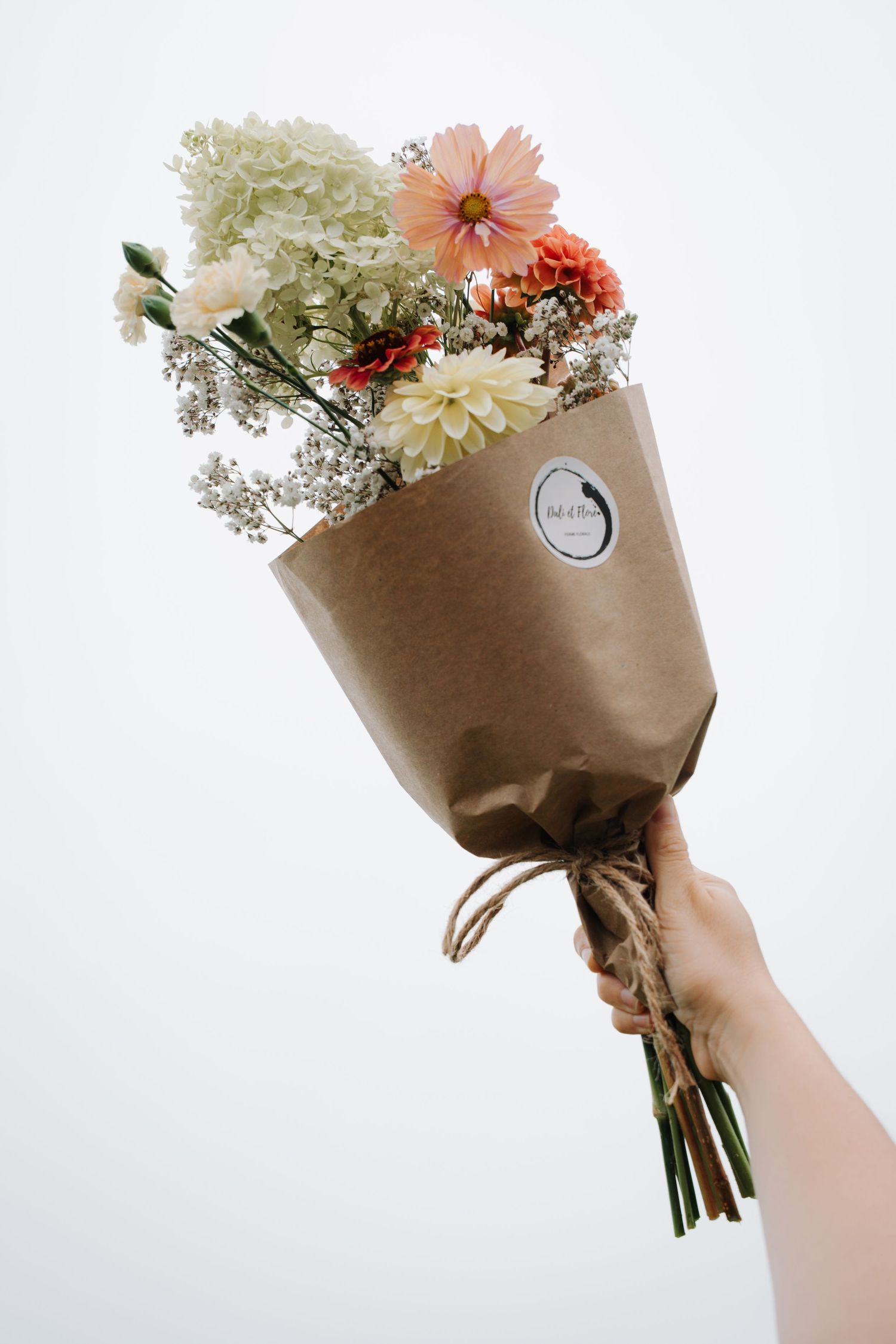 Hand holding a wrapped bouquet of mixed flowers including dahlias and hydrangeas.