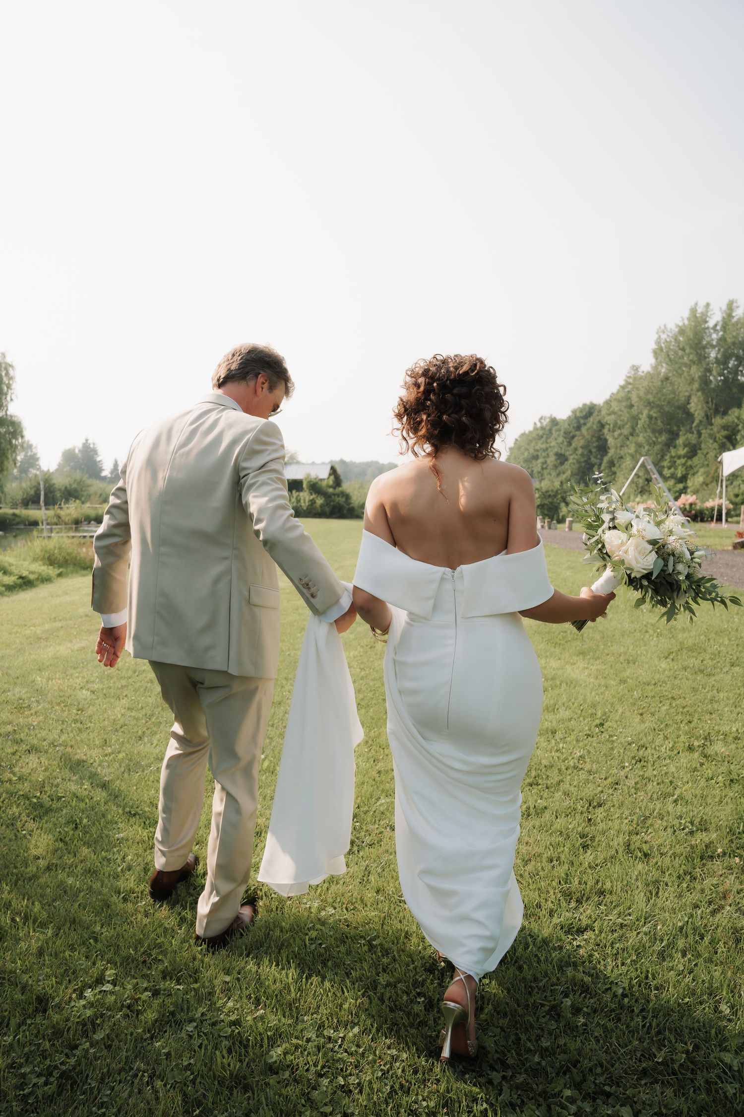 Bride and groom walking hand in hand across a green lawn after their outdoor wedding ceremony.