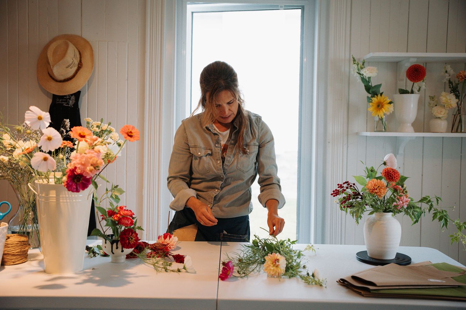 Woman arranging colorful fresh flowers on a white table in a bright floral studio.