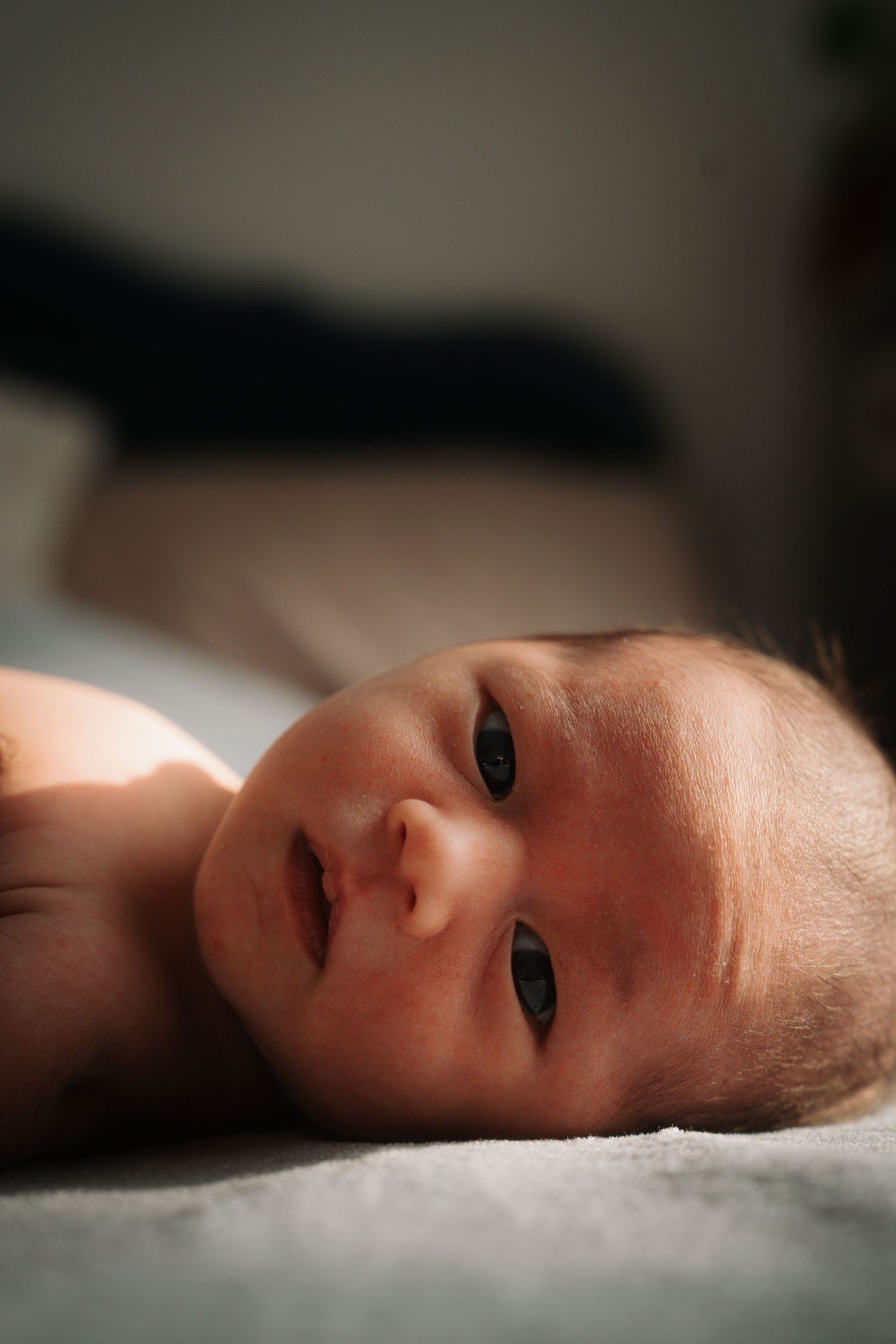 Close-up portrait of newborn baby lying on white blanket with soft natural lighting.