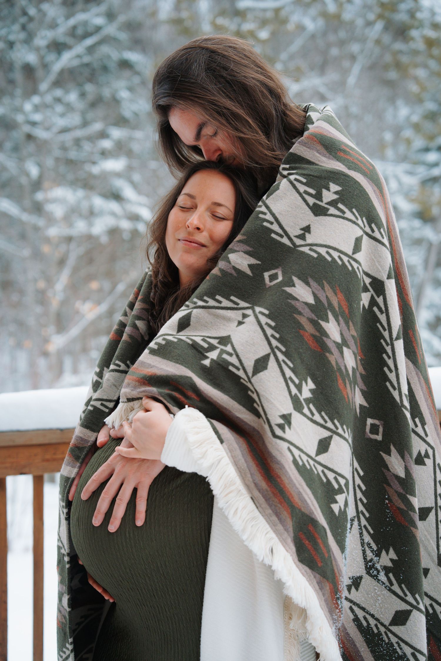 Couple wrapped in Aztec blanket sharing tender moment outdoors in snowy winter setting, maternity photo.