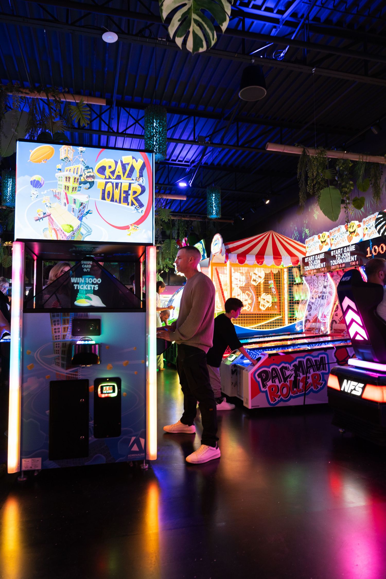Man plays Crazy Tower arcade game in a vibrant neon-lit arcade with tropical decor.