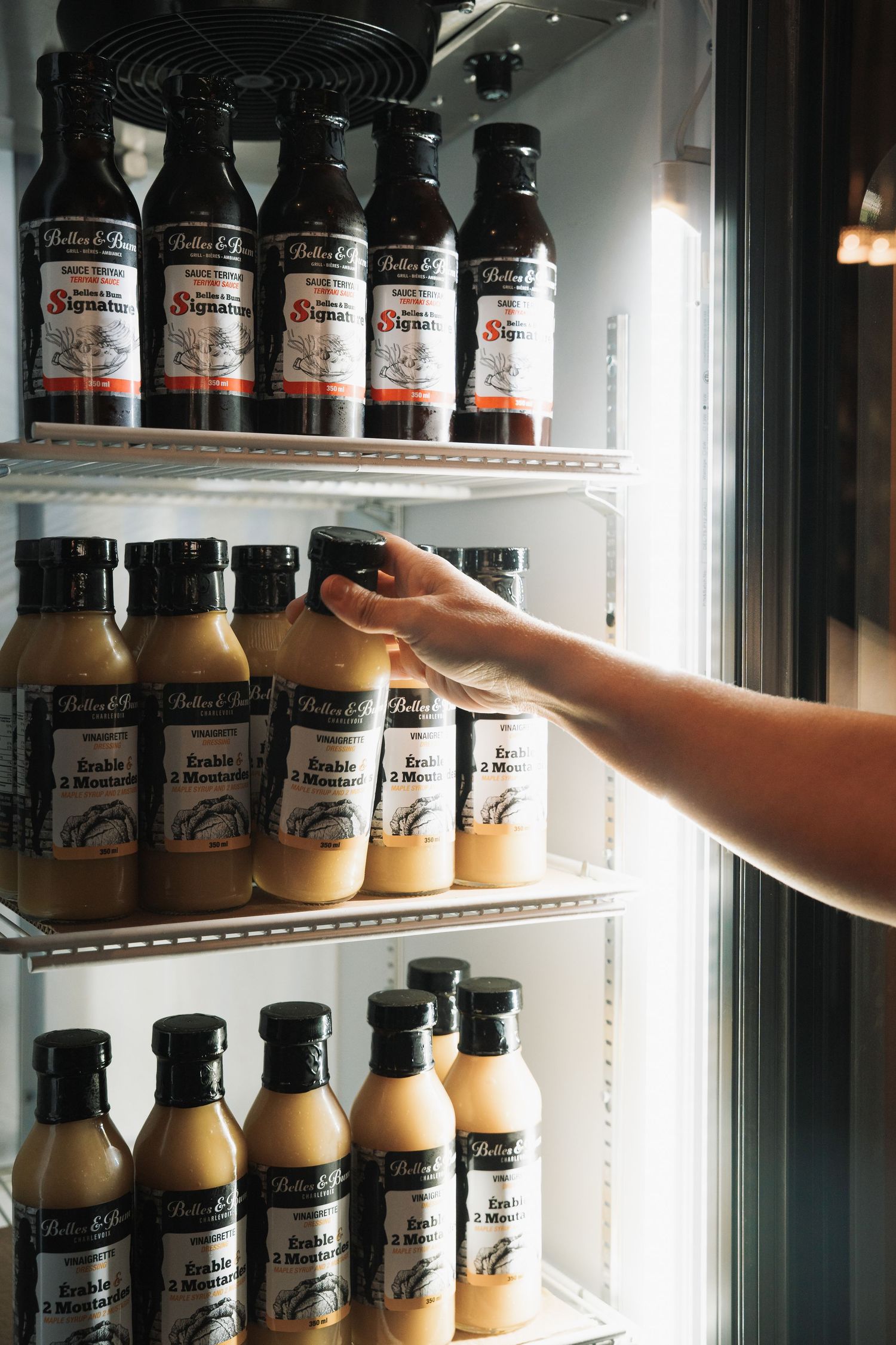 Hand reaching into a refrigerator stocked with bottles of Butter and Buns signature sauces.