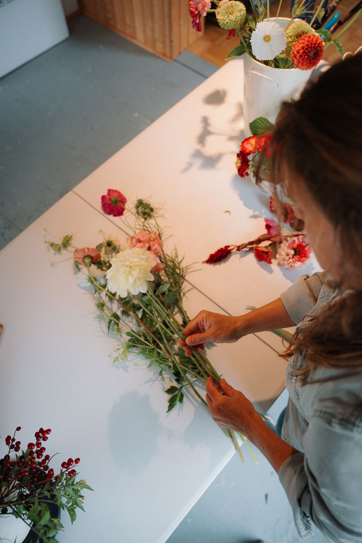 Florist arranging a variety of colorful flowers into a bouquet on a white table.