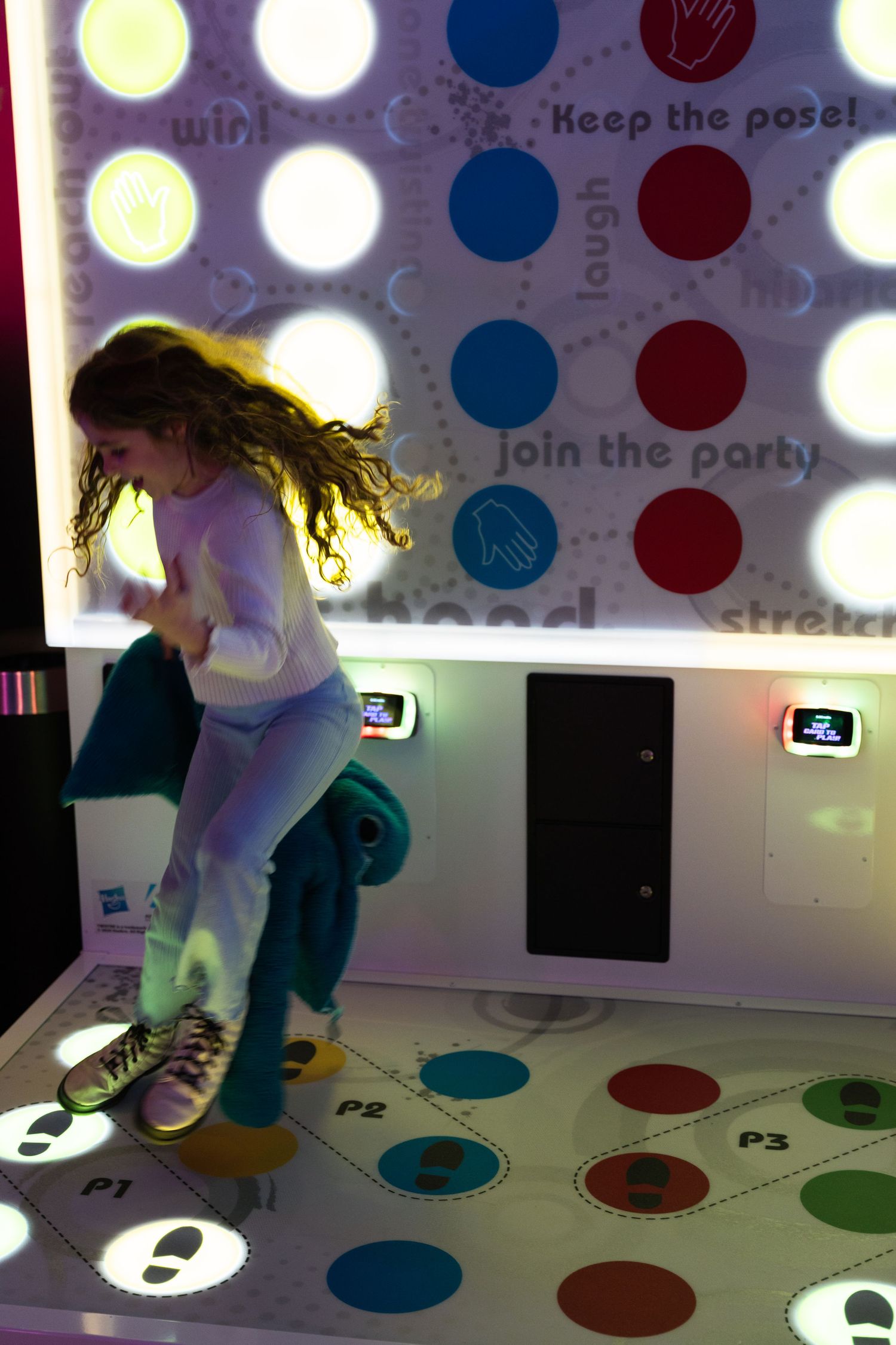 Young girl jumping on a dance mat arcade game with colorful polka dot projection screen.