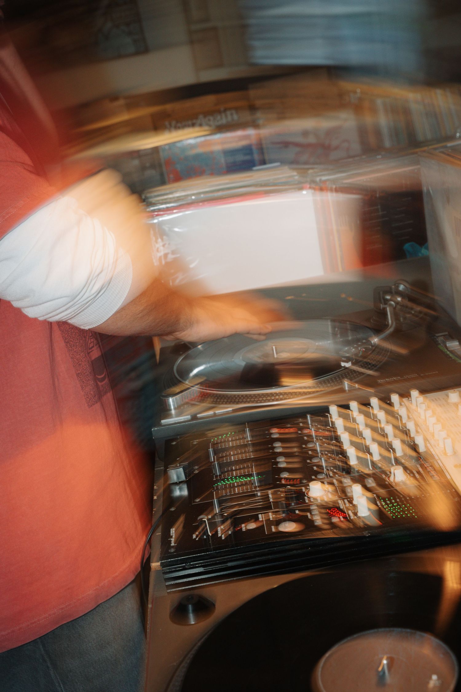 Motion blur photo of DJ mixing records on turntable and mixer equipment under warm lighting.