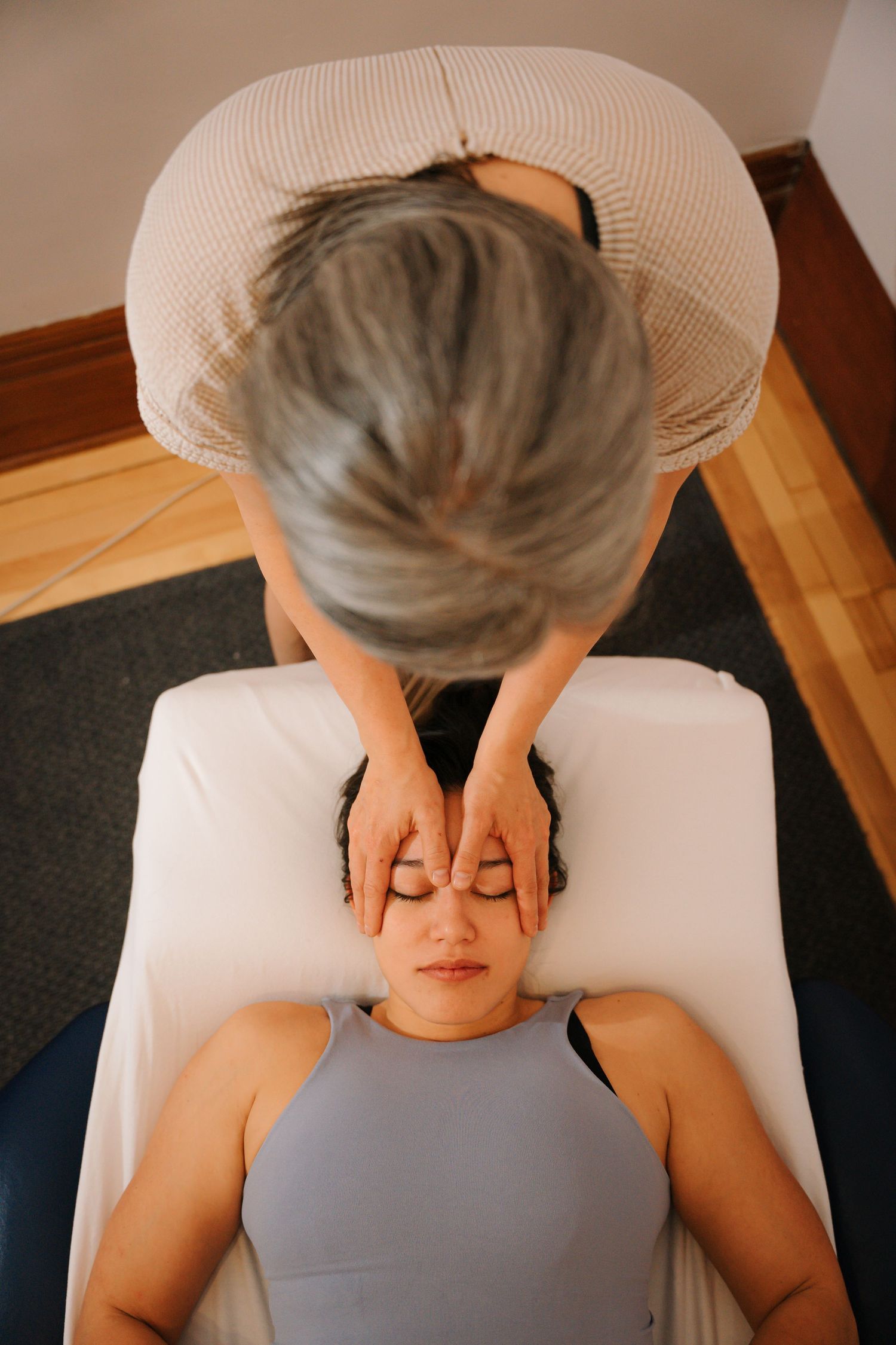Overhead view of a therapist performing a head massage on a relaxed woman lying on a treatment table.