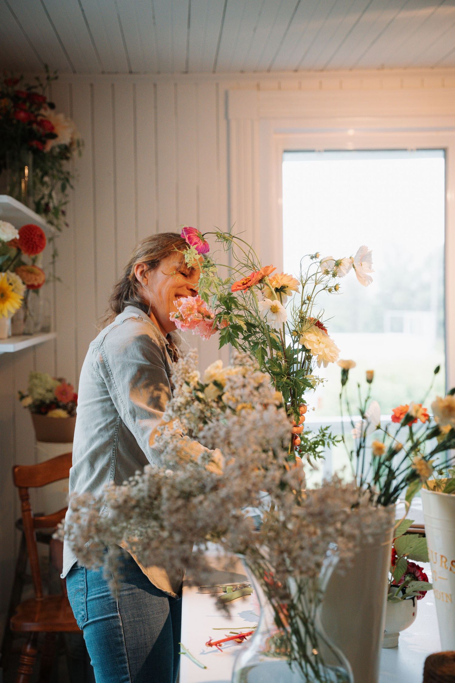 A florist arranges colorful fresh flowers in a bright white studio filled with blooms.