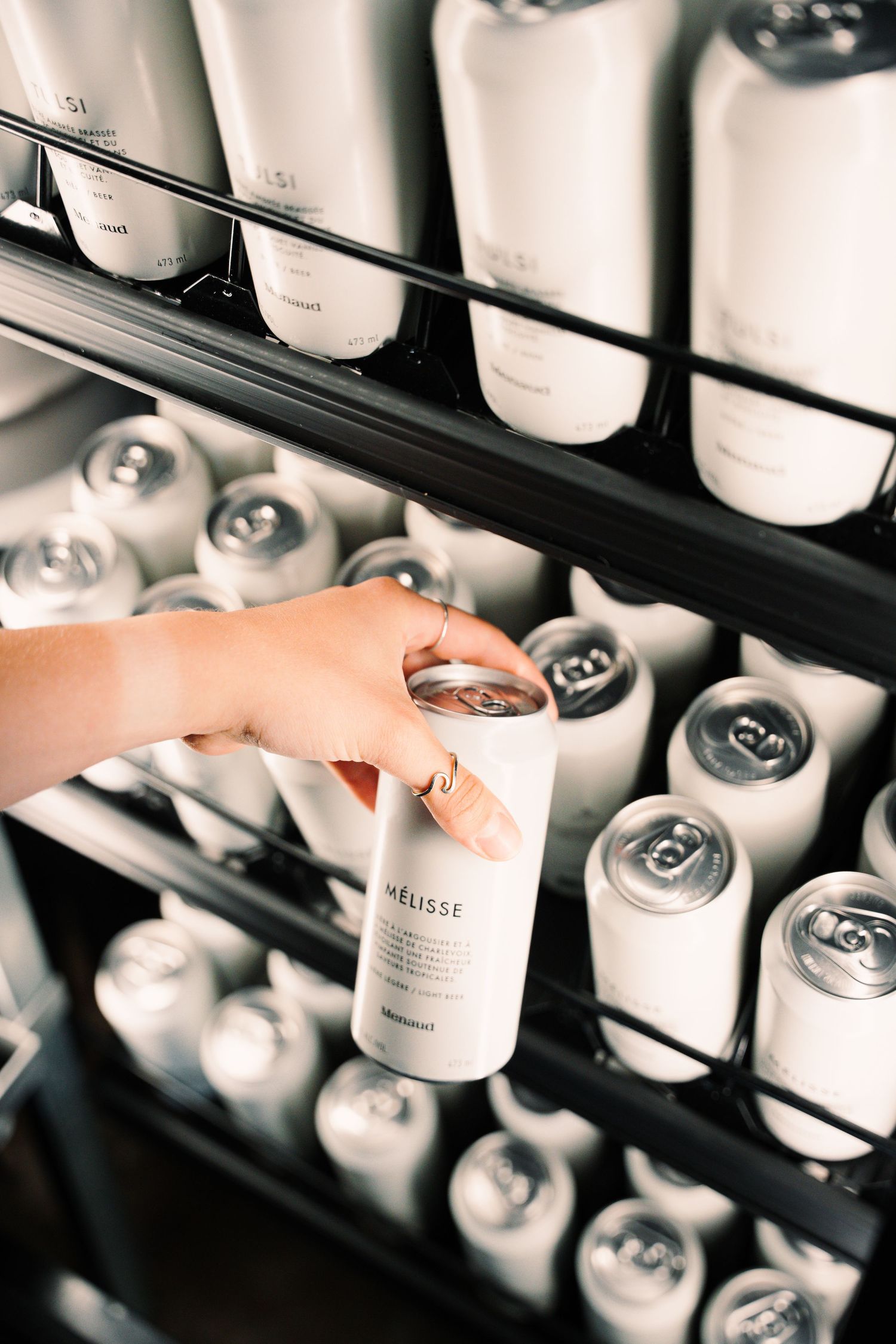 Hand picking a white can of Melisse beverage from a fully stocked black refrigerator shelf.