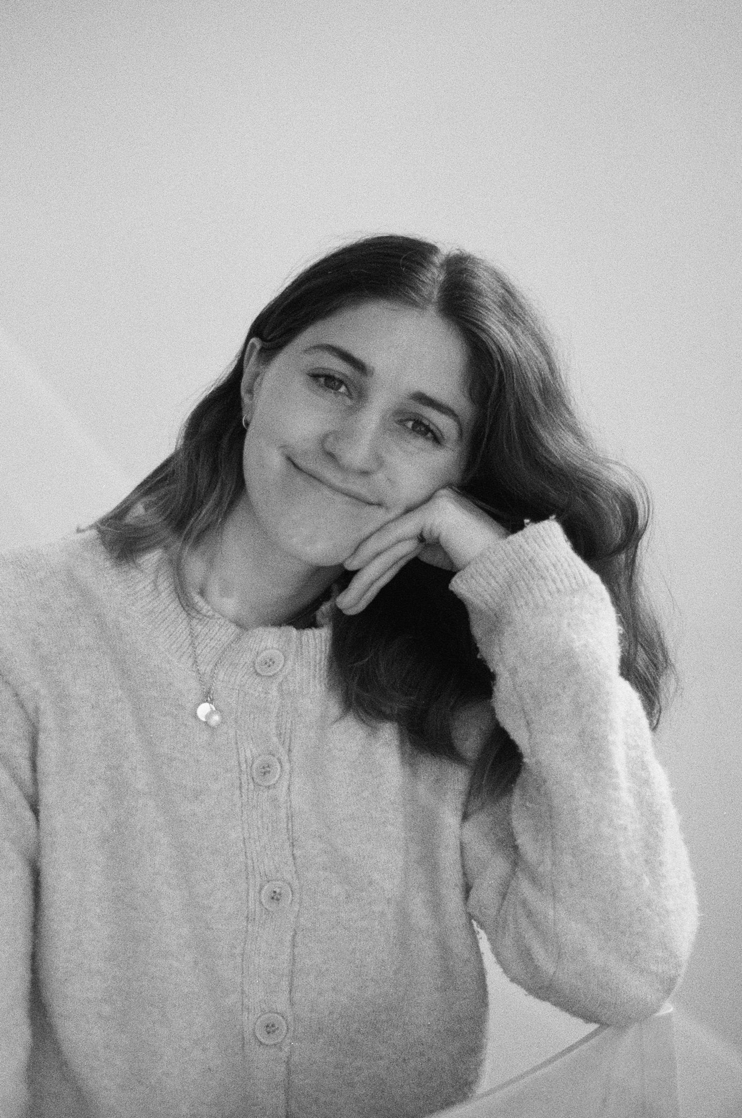 Black and white portrait of a young woman smiling with her hand resting on her chin.