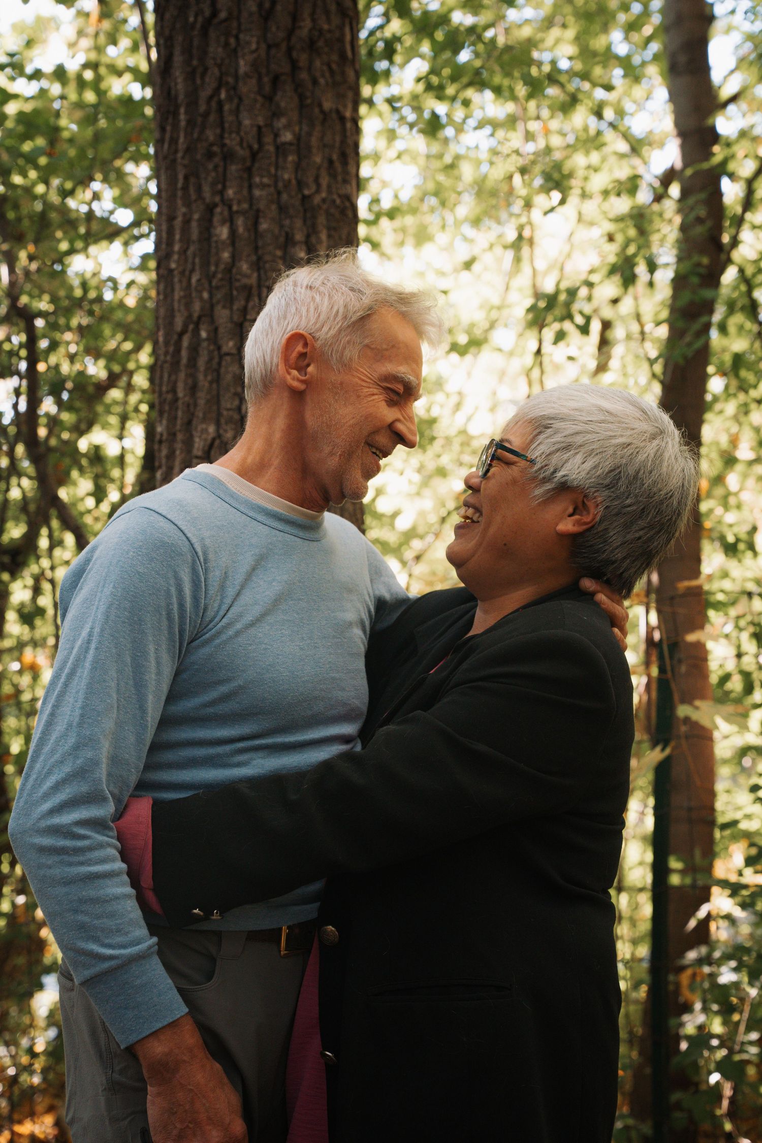 Happy senior couple embracing and smiling at each other in a lush green forest setting.