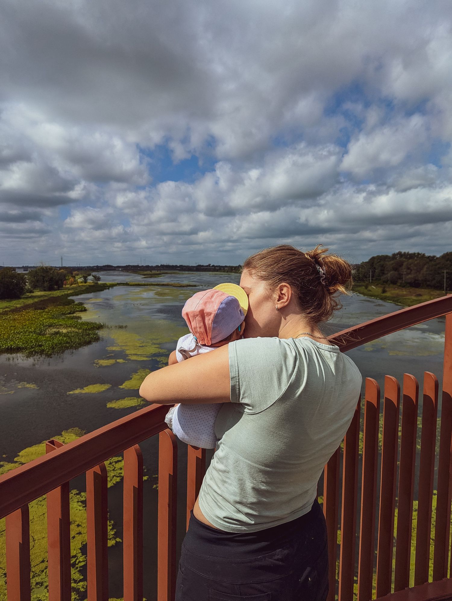 A mother tenderly holds her newborn baby on a scenic overlook above a wetland landscape.