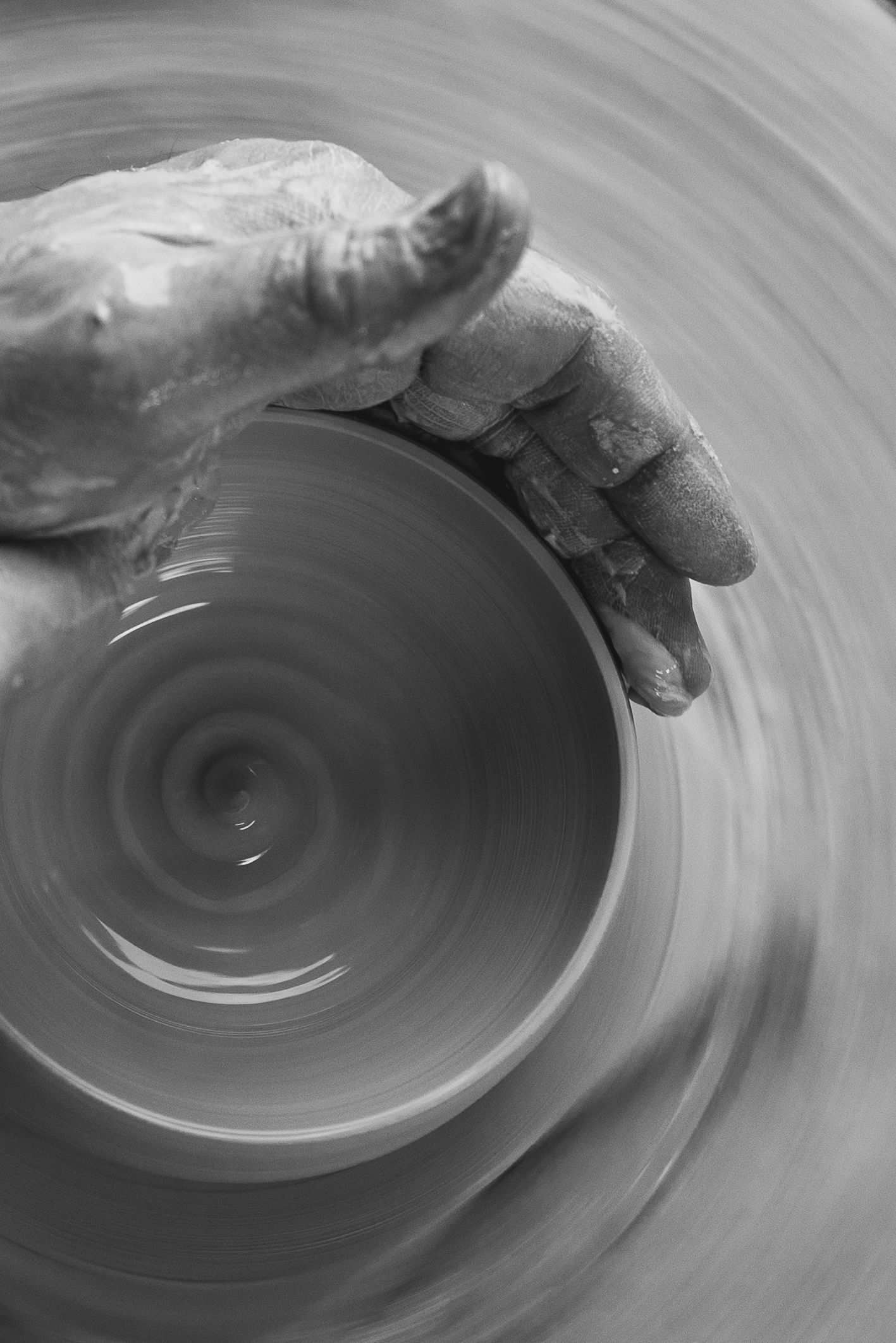 Black and white close-up of hands shaping a clay bowl on a spinning pottery wheel.
