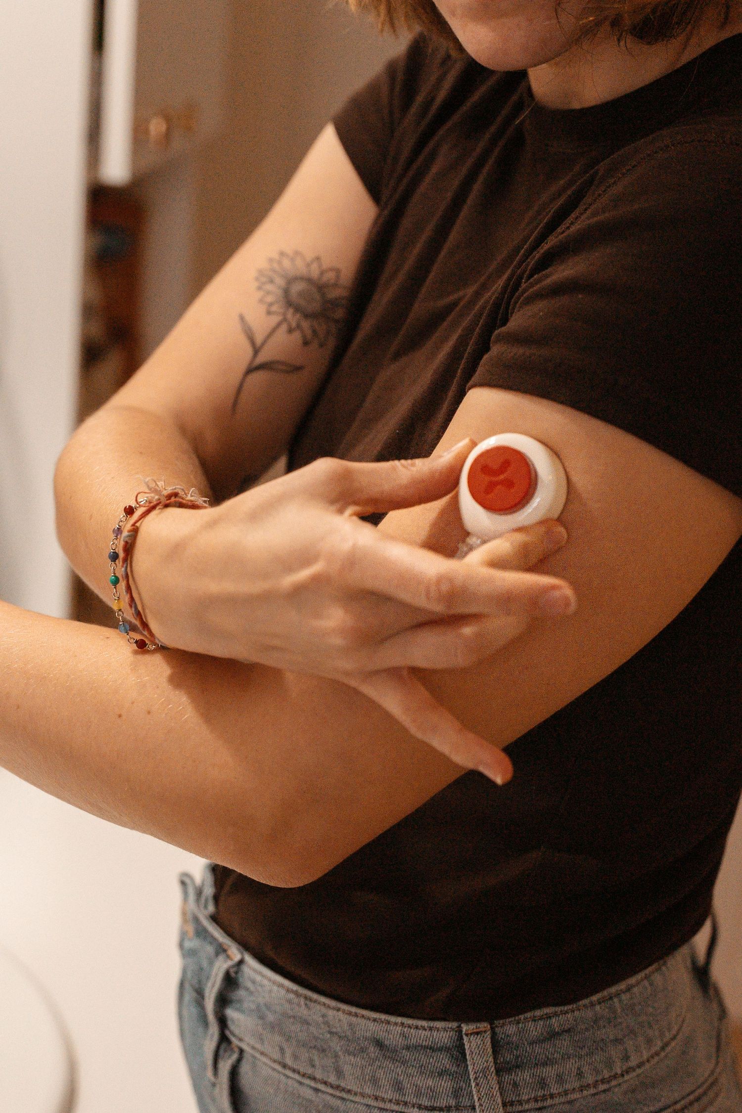 Person pressing a white CGM applicator onto their upper arm, tattoo visible on bicep.