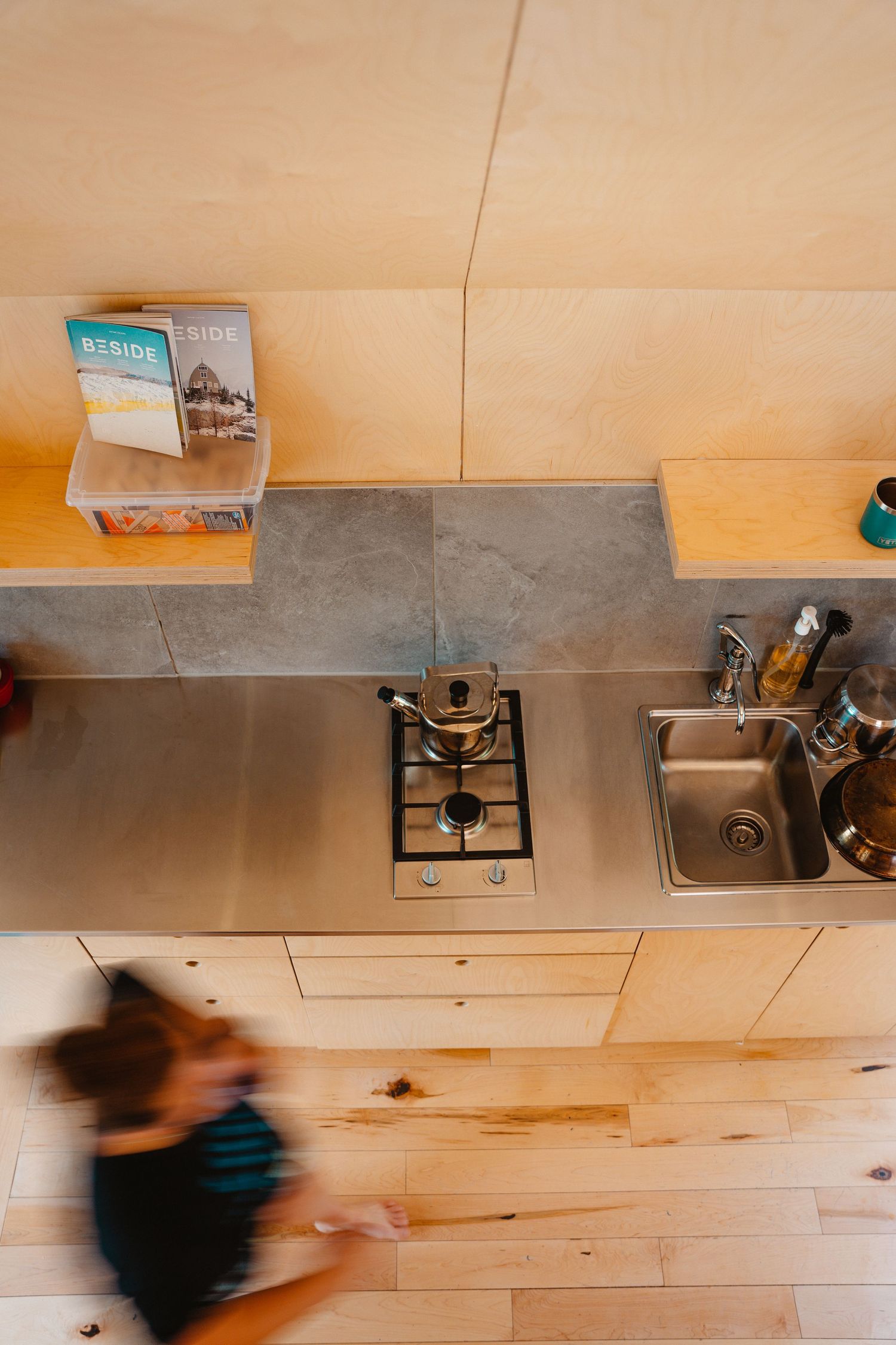 Aerial view of a compact stainless steel kitchen with gas stove and sink in a tiny home.