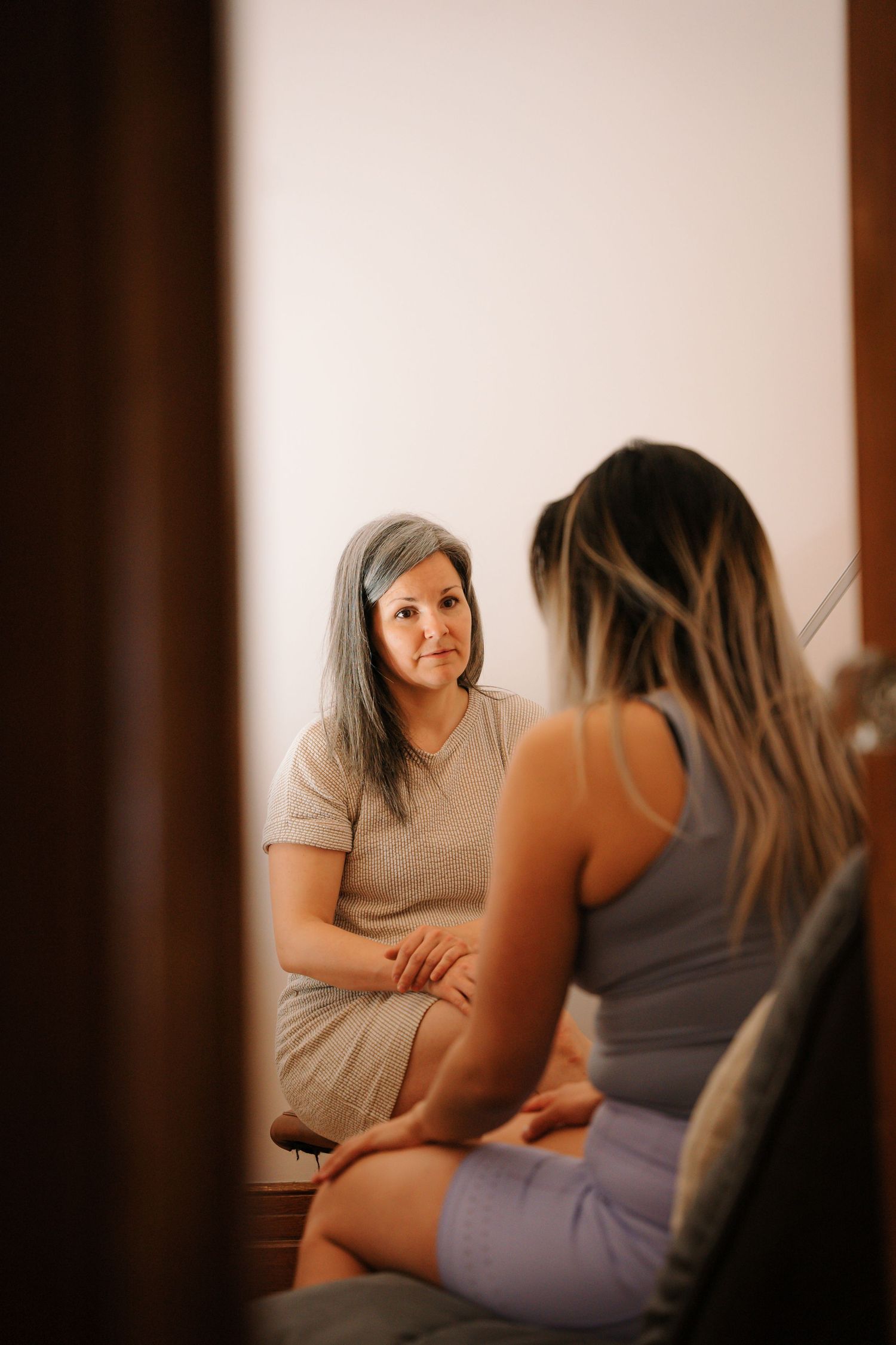 Female therapist in consultation with a patient, sitting face-to-face in a warm clinical setting.