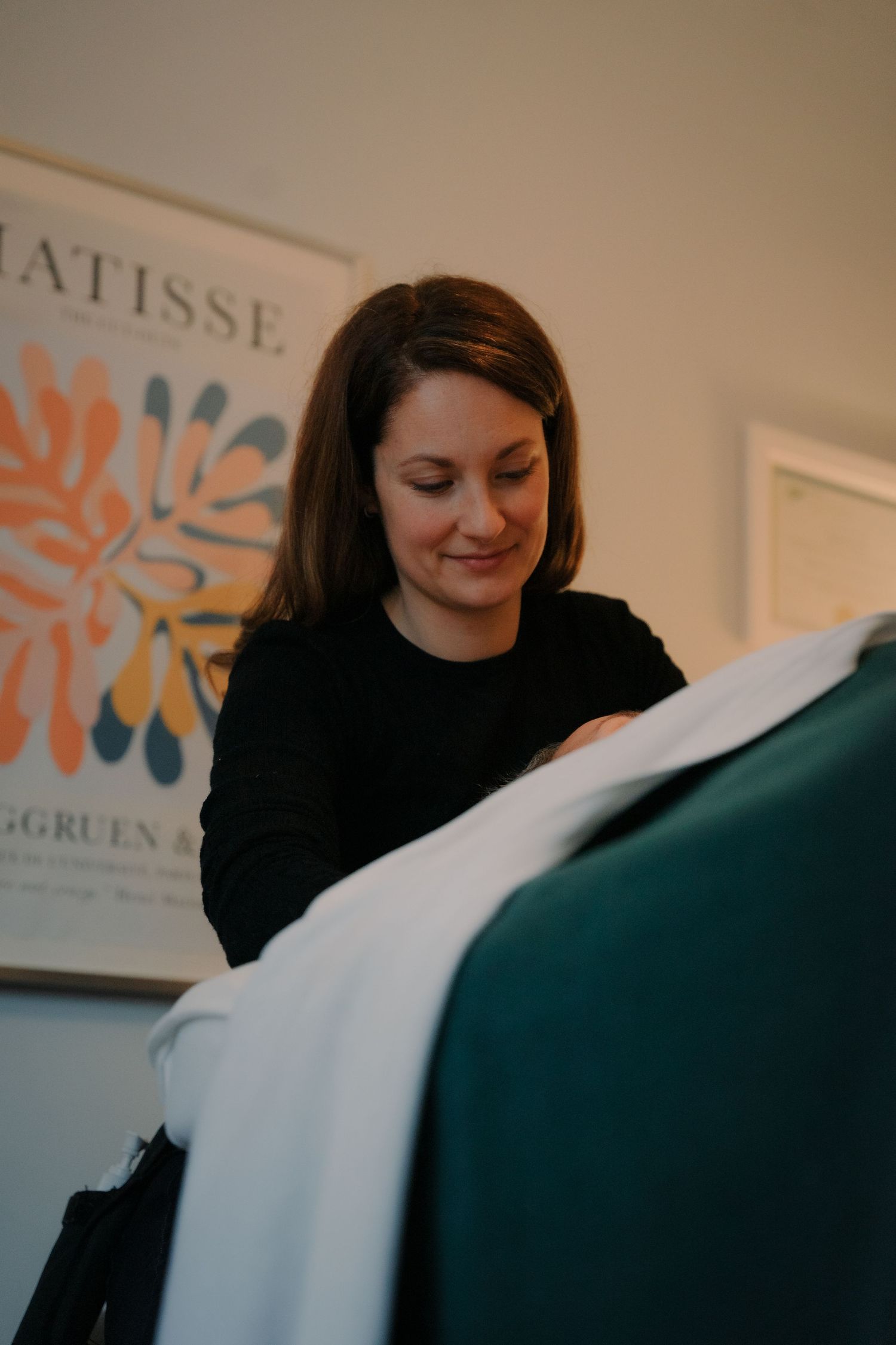 Smiling female massage therapist preparing treatment table with Matisse poster in background.