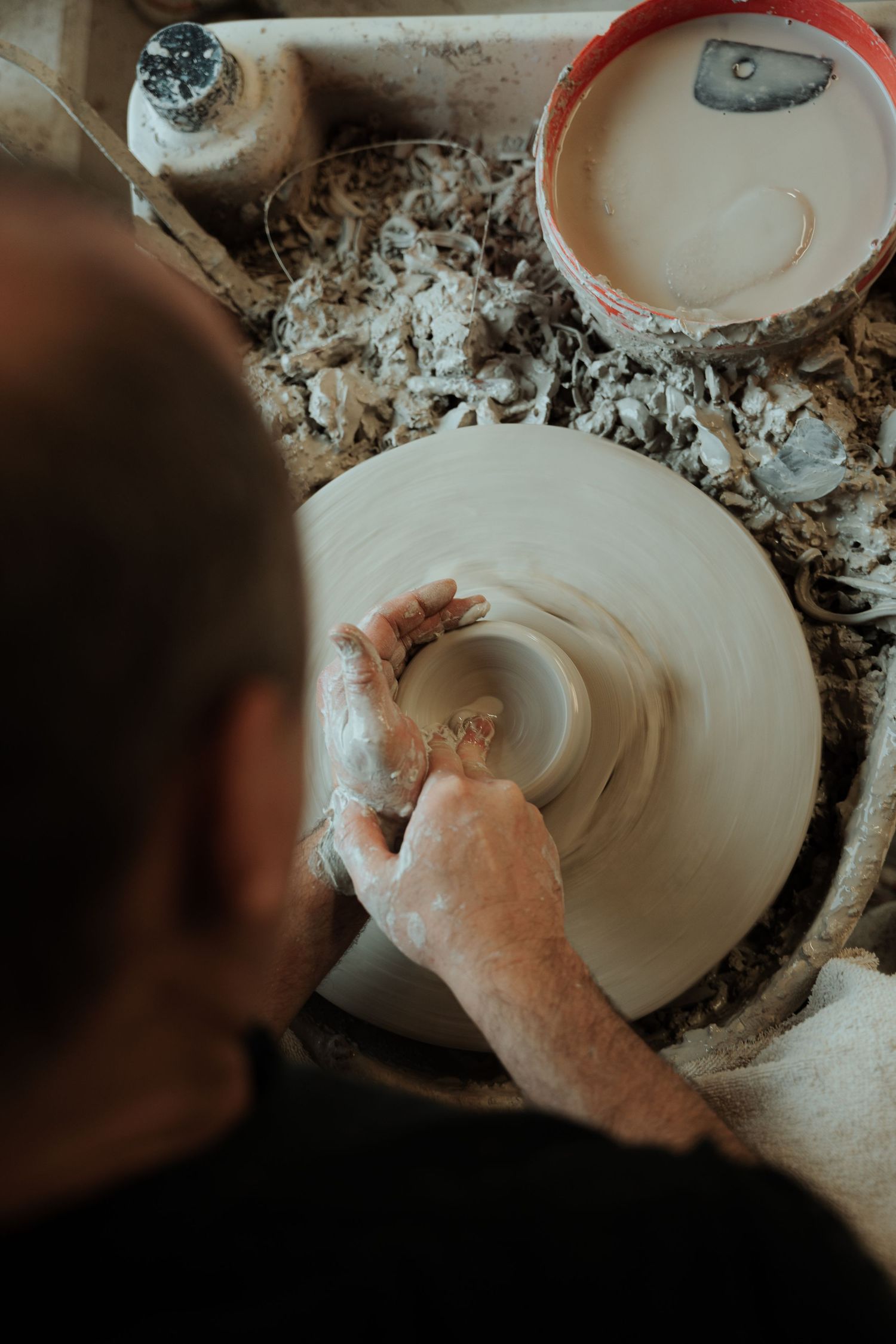 Overhead view of a potter shaping clay on a spinning wheel with clay shavings around.