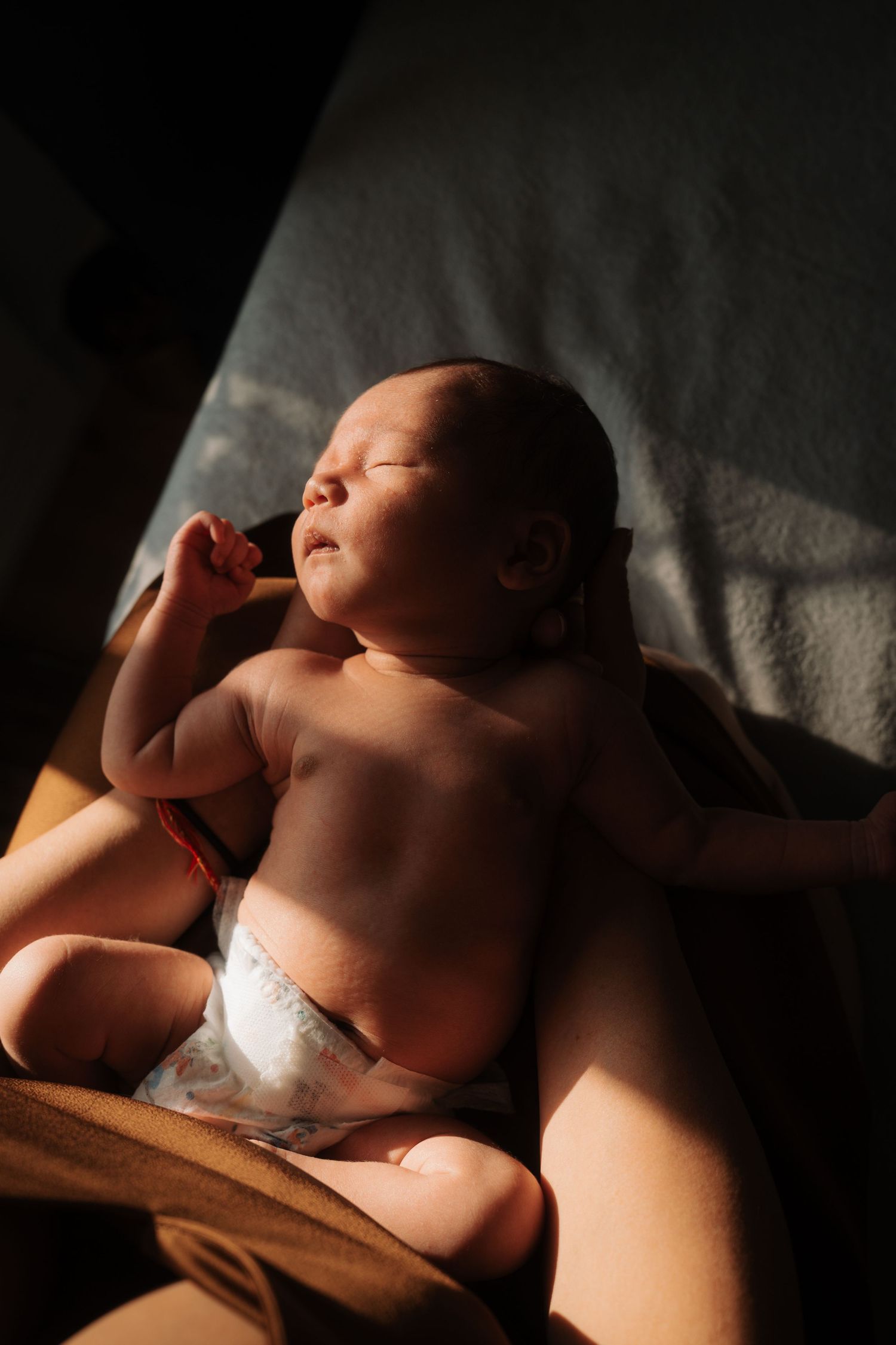 Newborn baby sleeping peacefully in warm sunlight wearing a diaper.