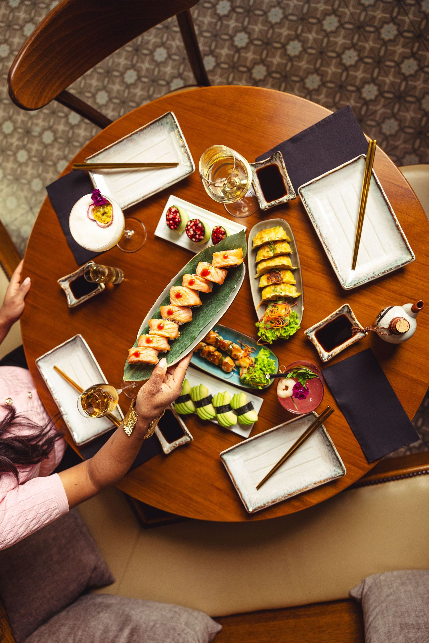 Overhead view of multiple sushi plates and dishes arranged on wooden dining table.