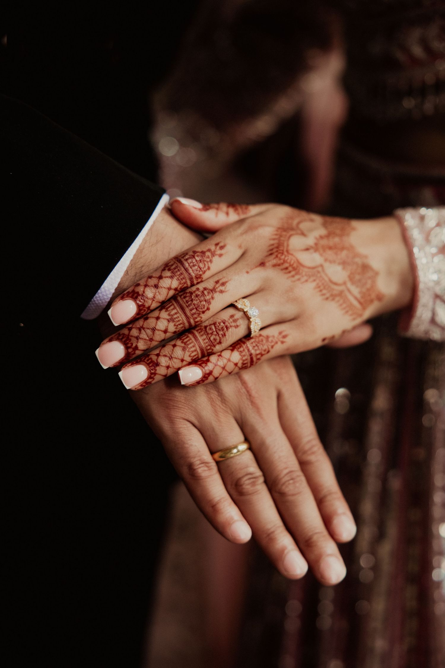 Close-up of hands adorned with intricate henna designs and wedding rings.