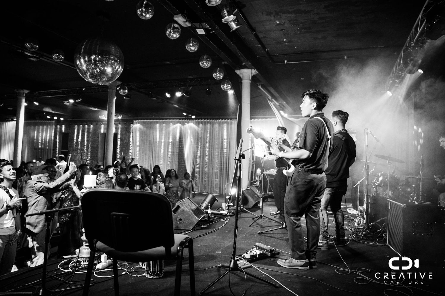 Black and white shot of band performing on stage with crowd visible in venue.