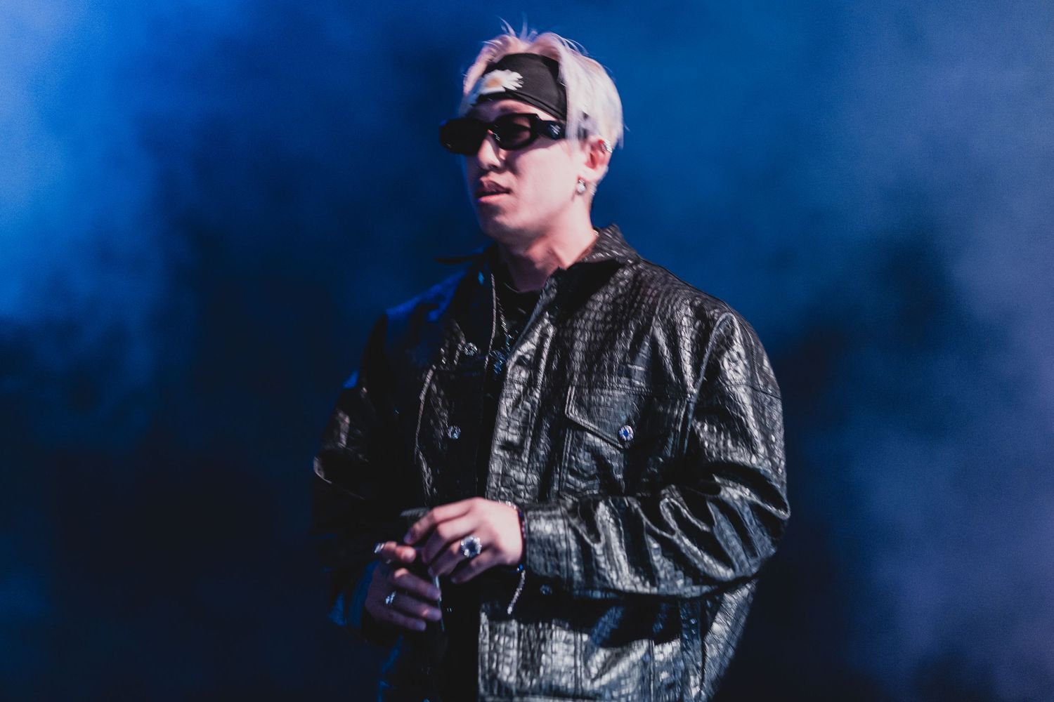 Performer in black leather jacket on stage with blue atmospheric lighting.
