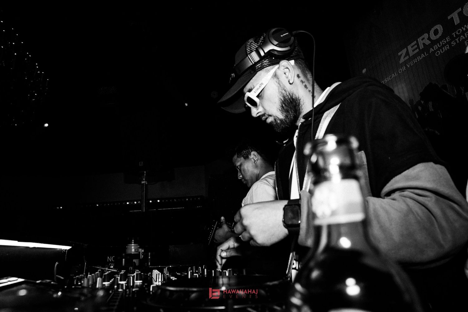 Black and white photo of DJ working turntables with dramatic lighting in club setting.