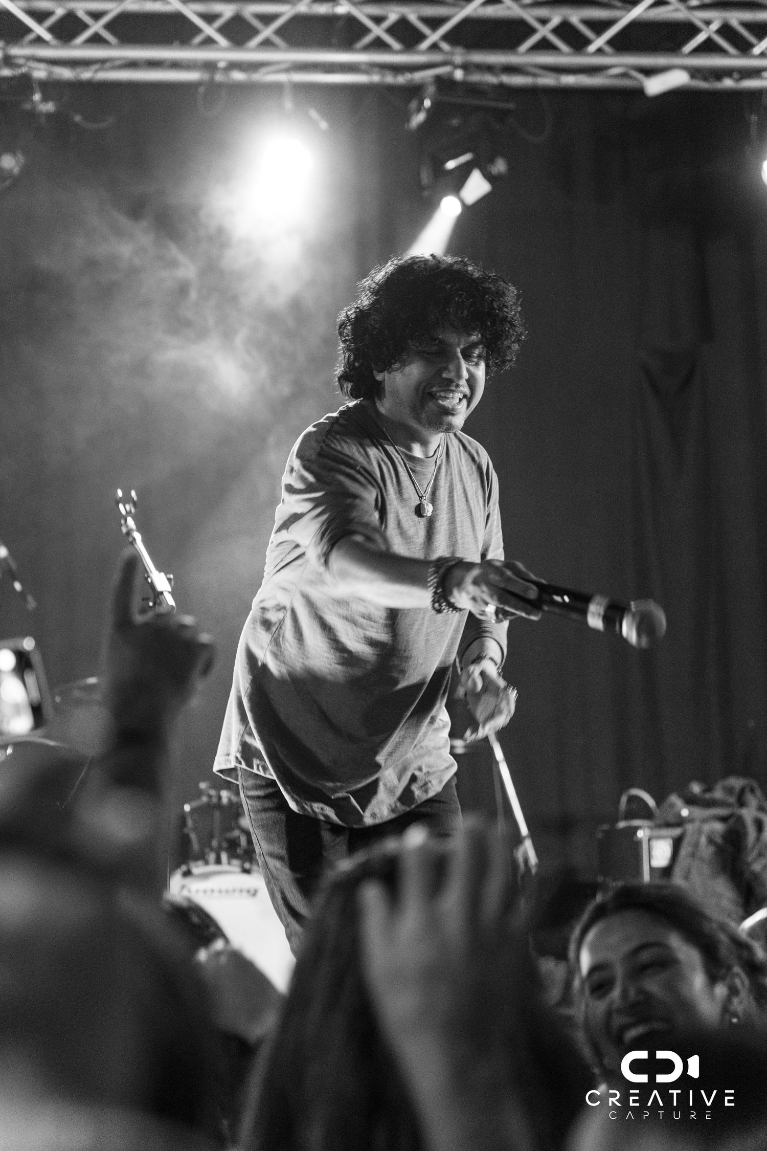 Black and white concert photo capturing performer in mid-performance with microphone on stage.