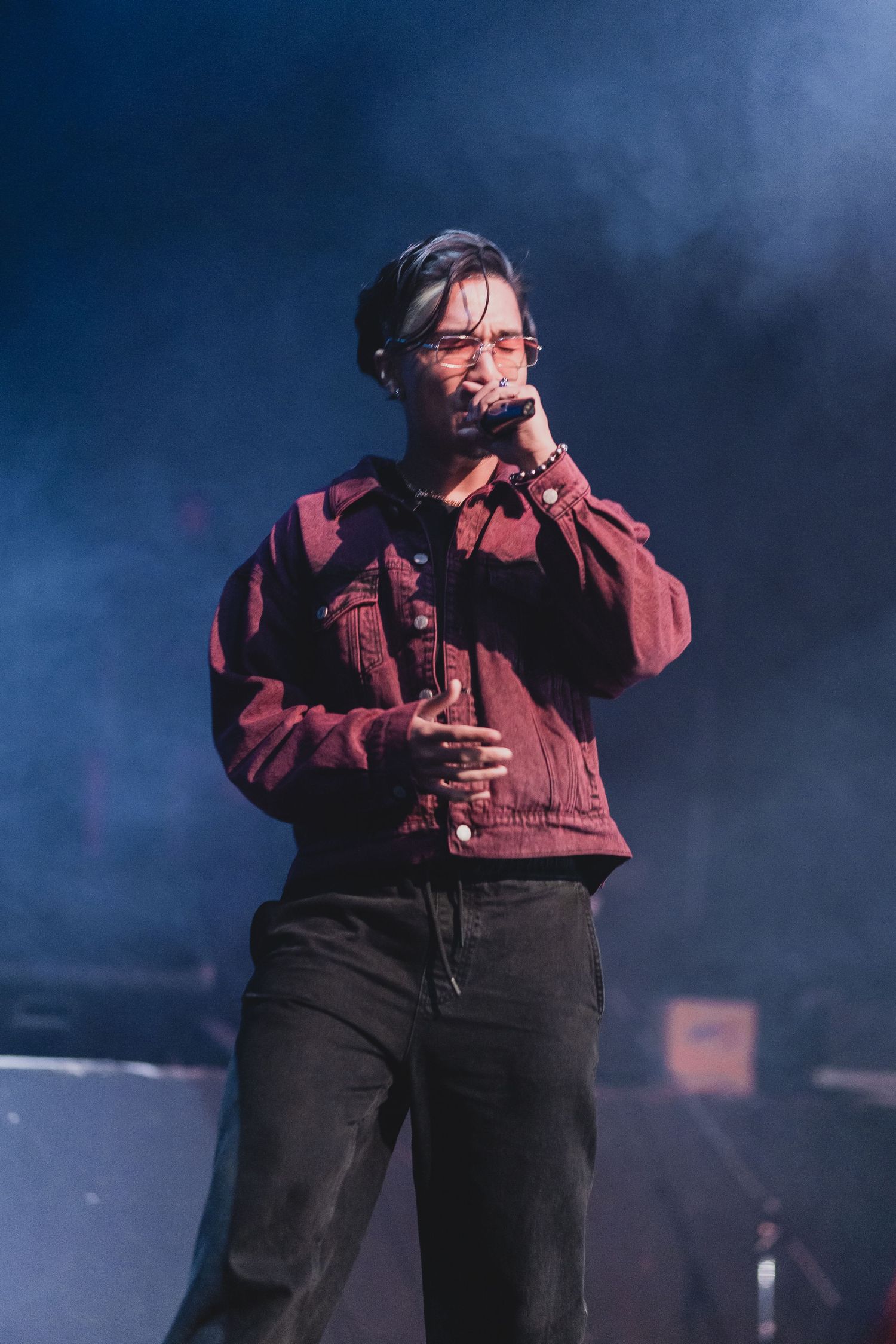 Singer in red jacket performing on misty stage with dramatic lighting.