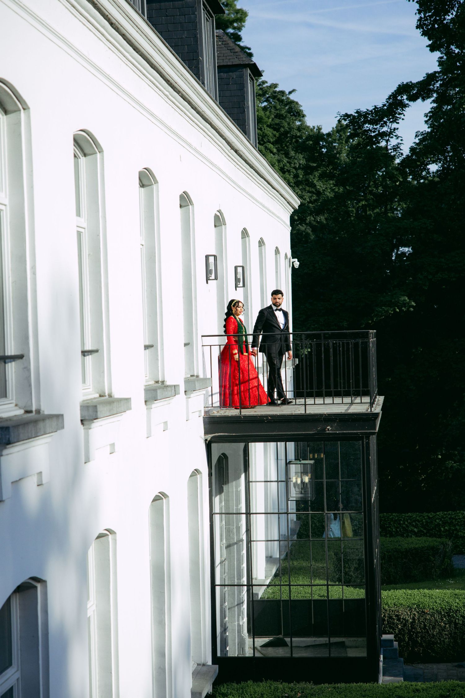 White building exterior with balcony and figures visible against bright sky.