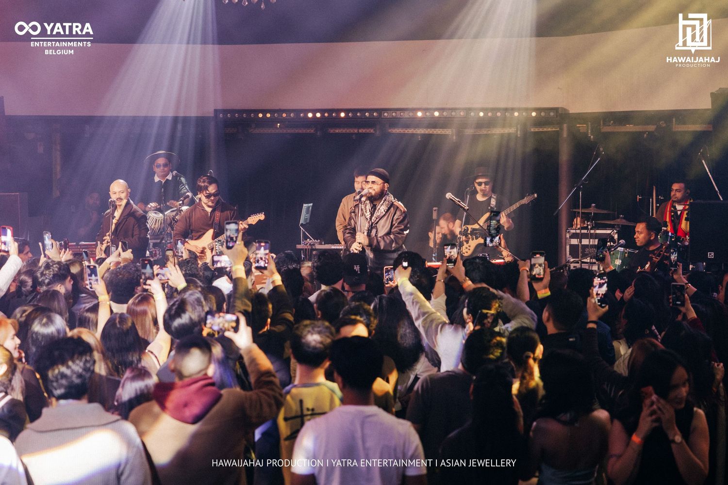 Concert crowd raises hands in excitement as stage lights illuminate the enthusiastic audience.
