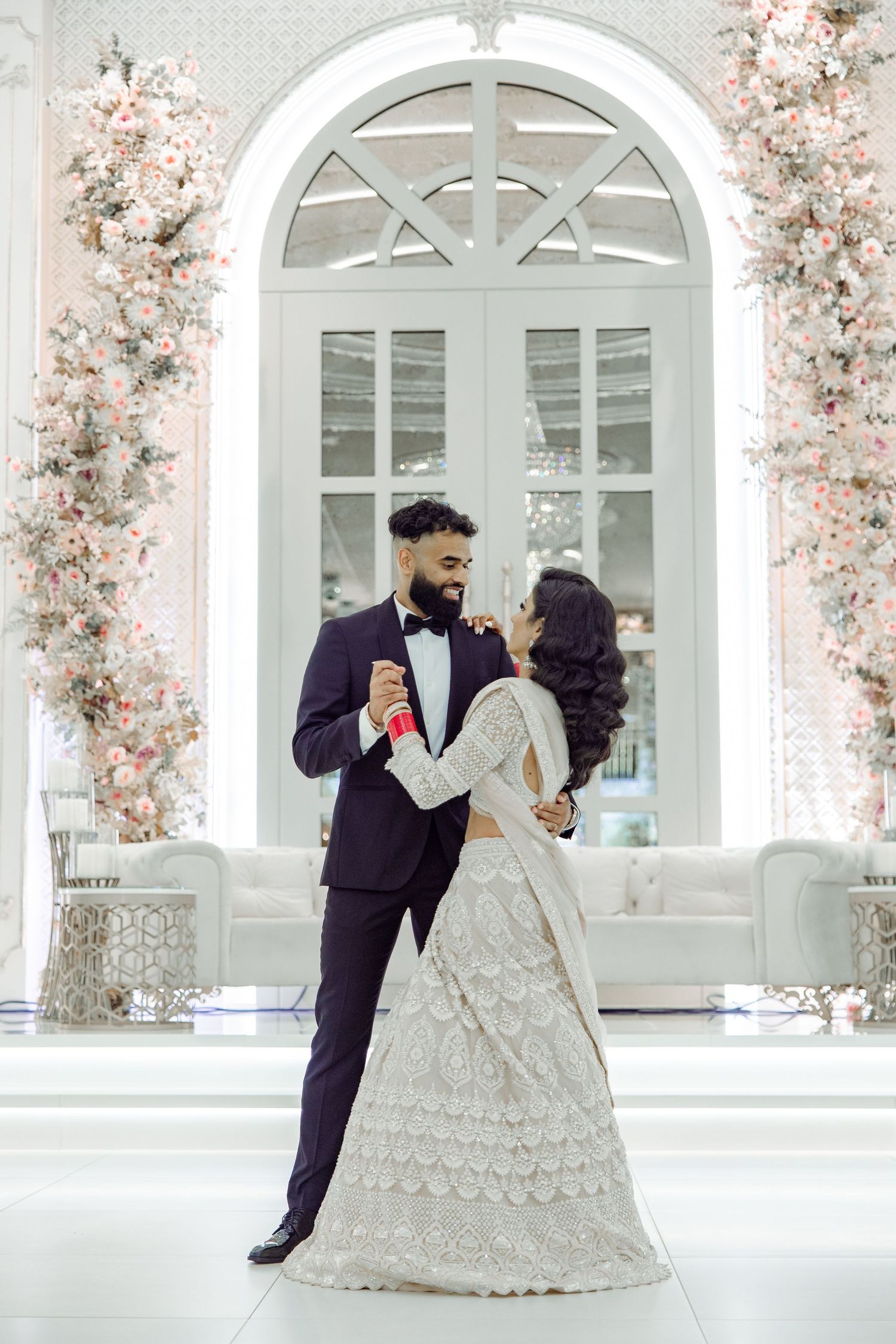 Wedding photoshoot in elegant white venue with arched windows and floral decorations.