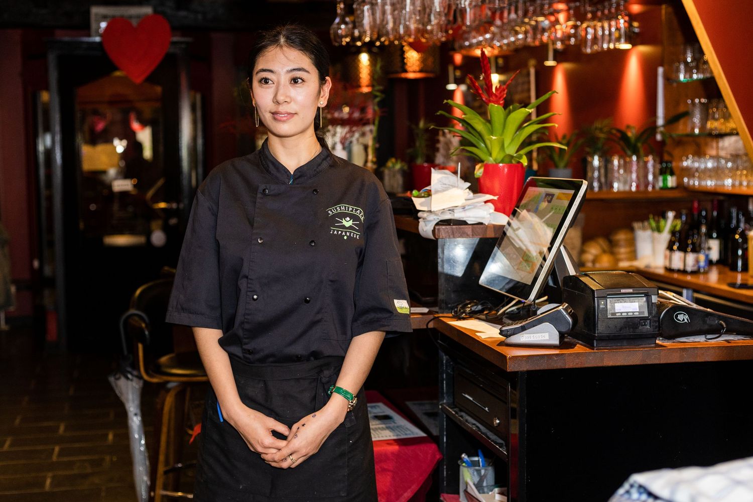Restaurant staff in black uniforms stand behind a warmly lit bar with bottles and glassware.