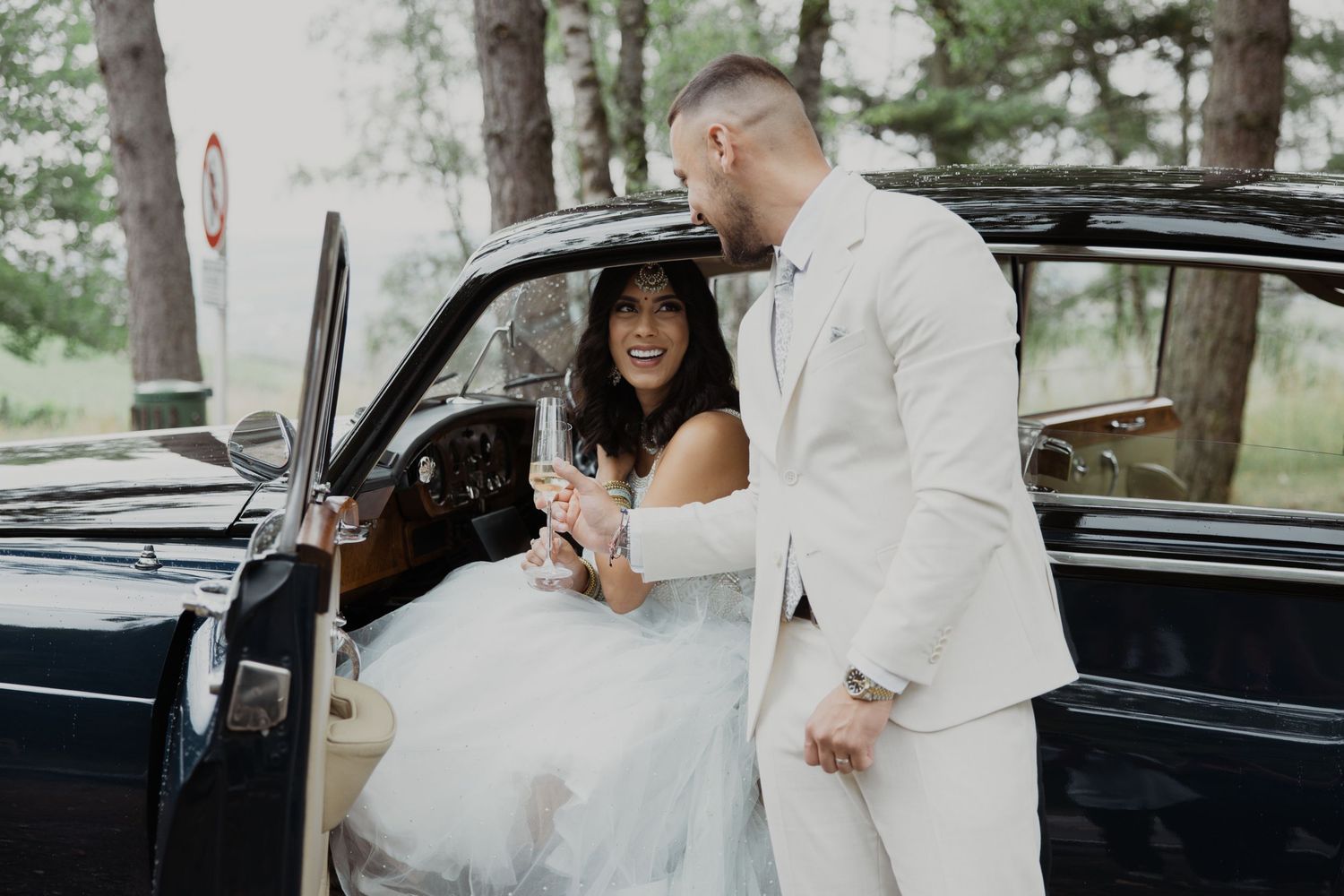 Wedding couple sharing intimate moment next to vintage black car.