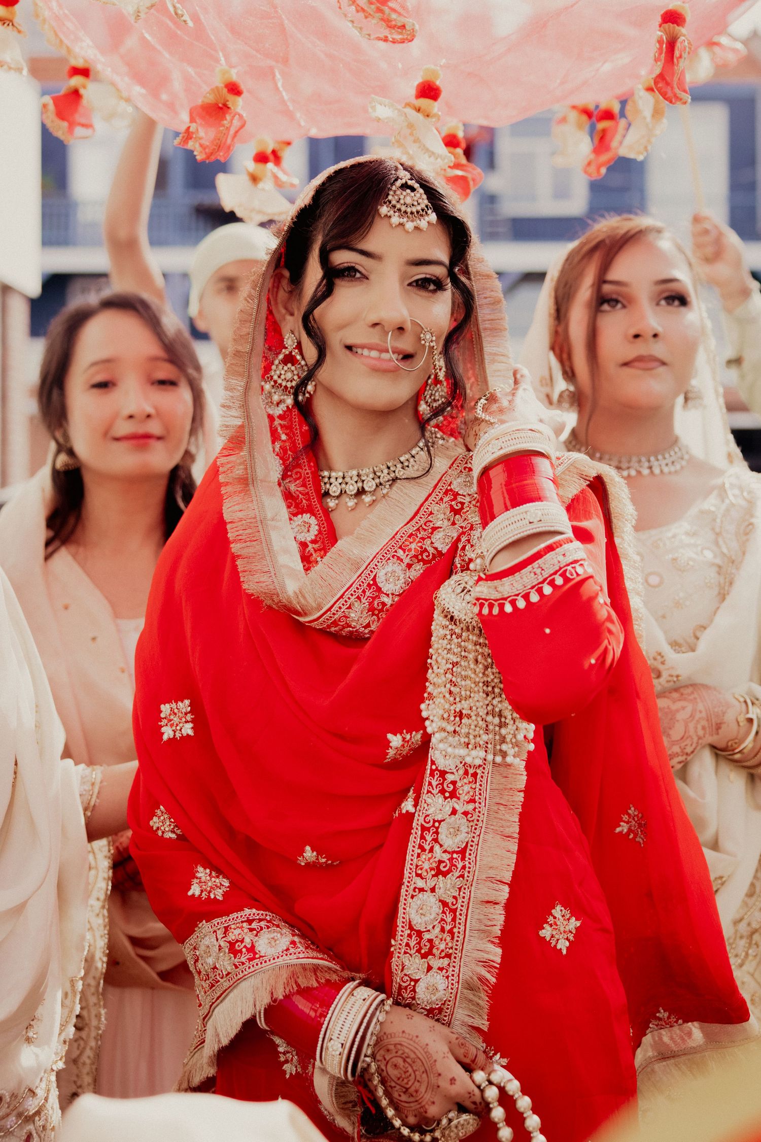 Wedding party in red and white traditional Indian attire celebrates with decorative fans.