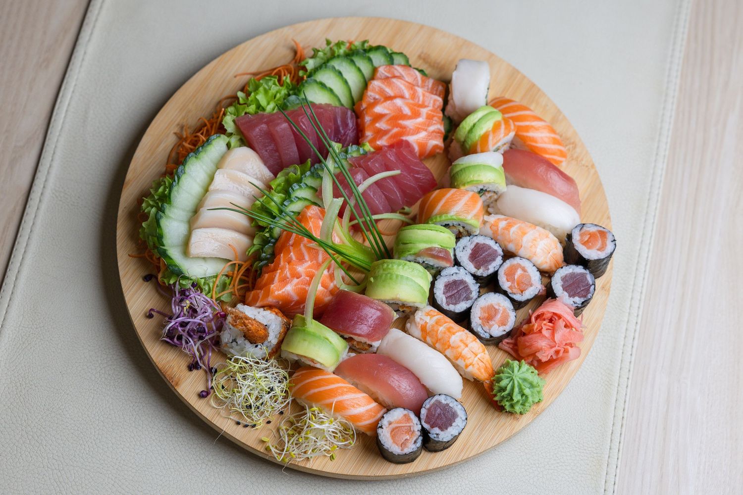Large sushi and sashimi platter with fresh fish, vegetables and garnishes on wooden board.