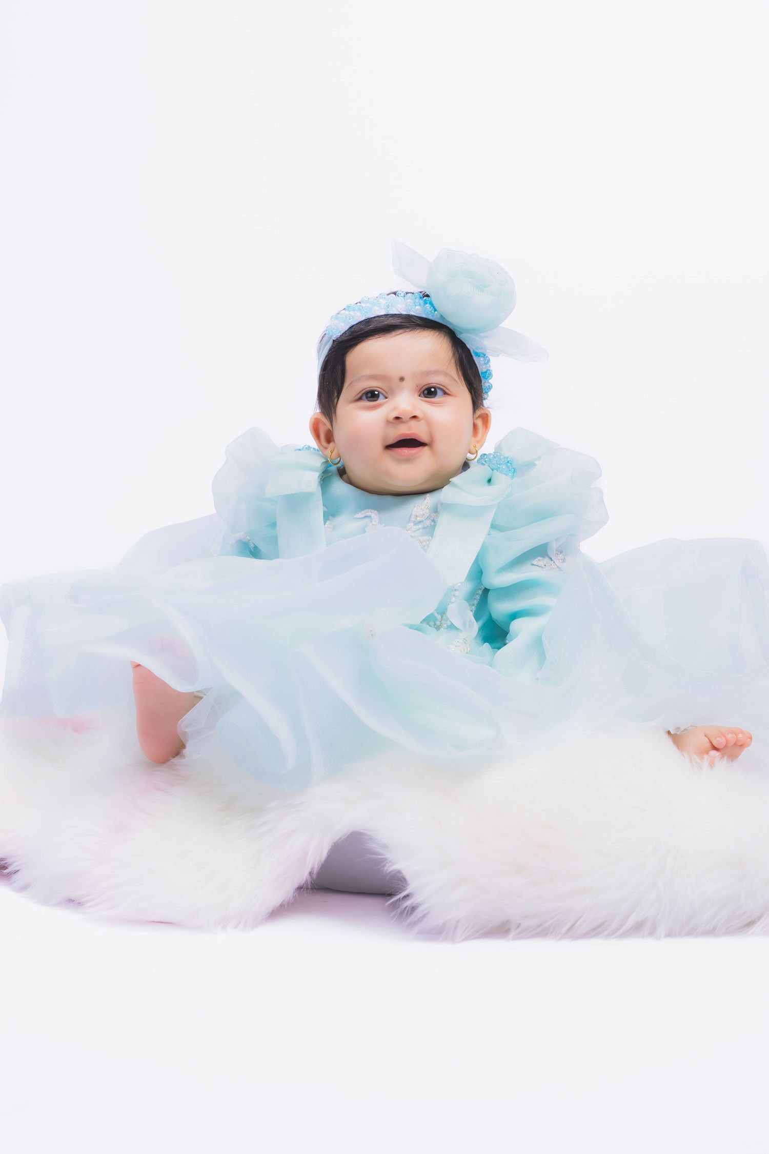 Baby wearing light blue tulle outfit smiles while lying on white background.