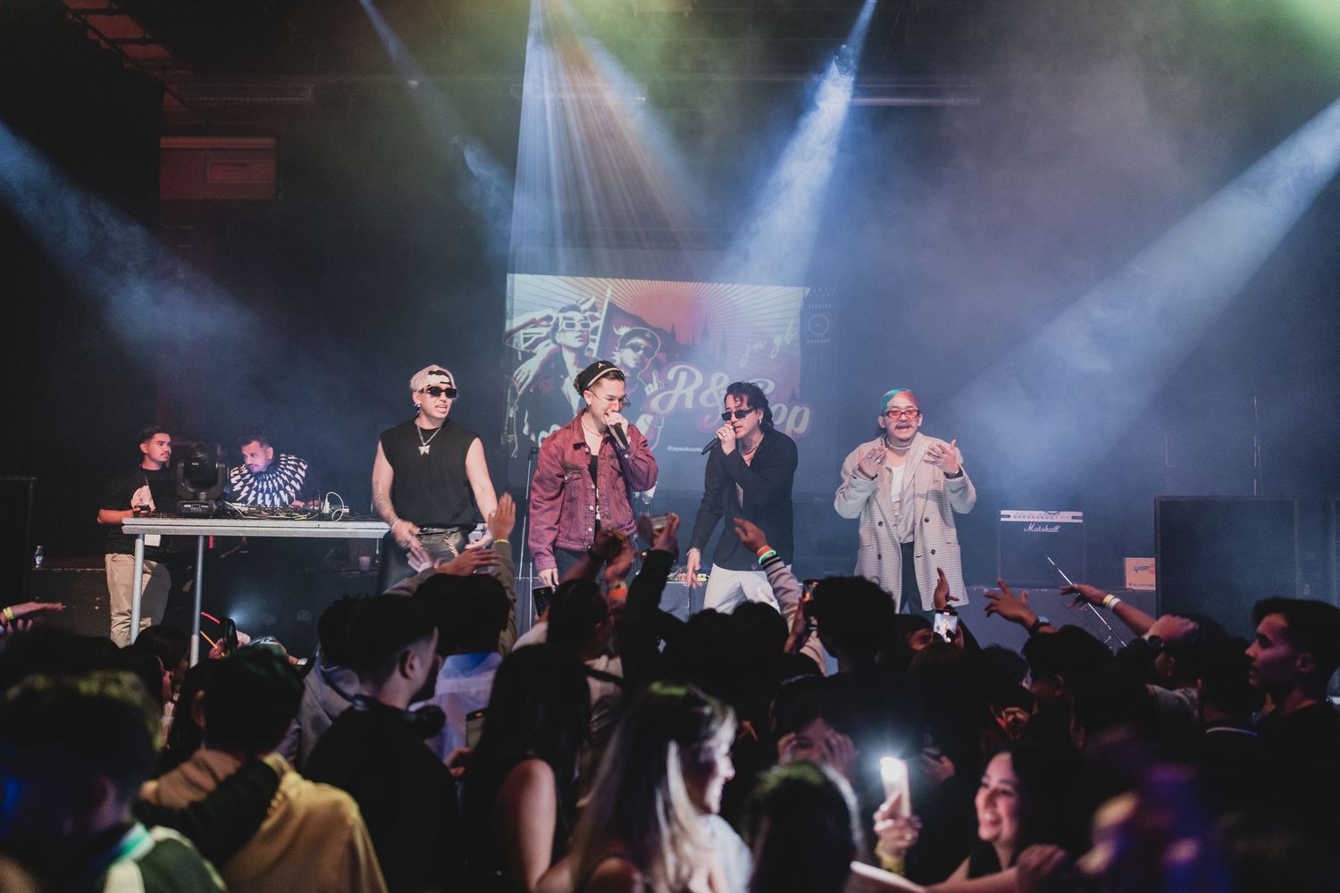 Concert performers on stage with dramatic spotlights and crowd in foreground.