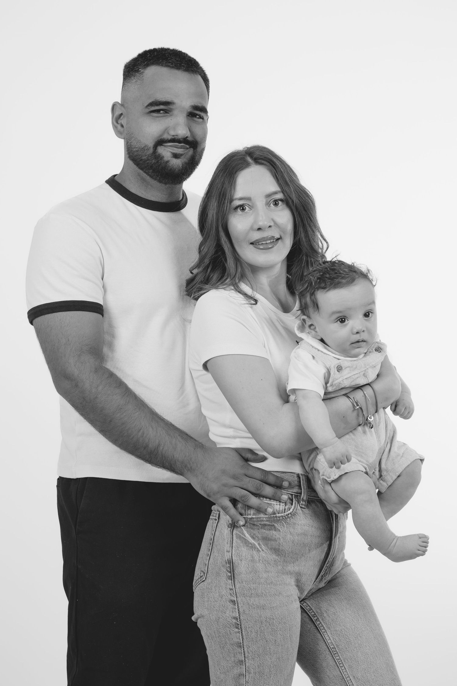 Family in coordinated white and black outfits poses together against white studio background.