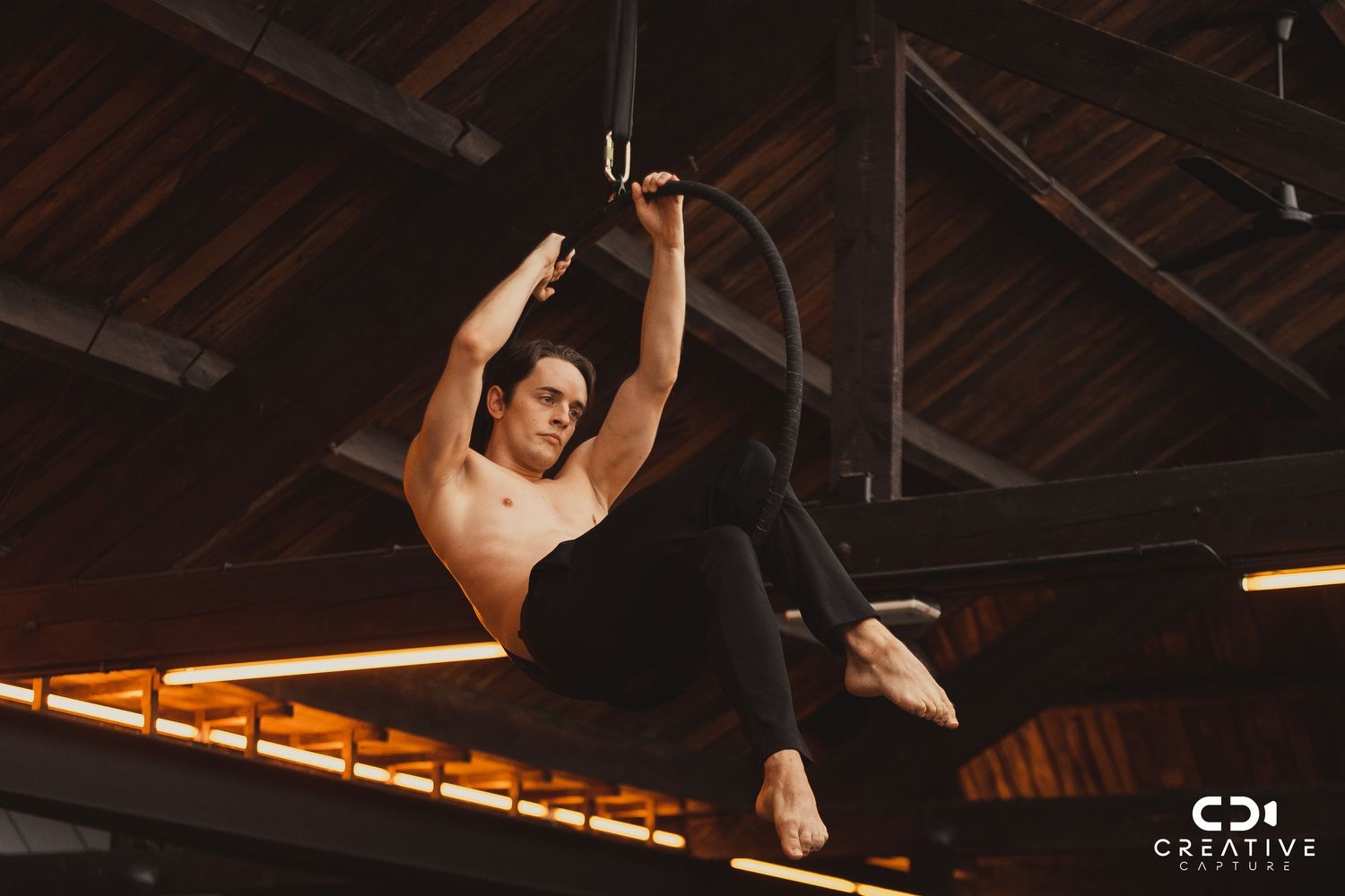 Aerial acrobat executing a dramatic pose while suspended from ceiling rigging.