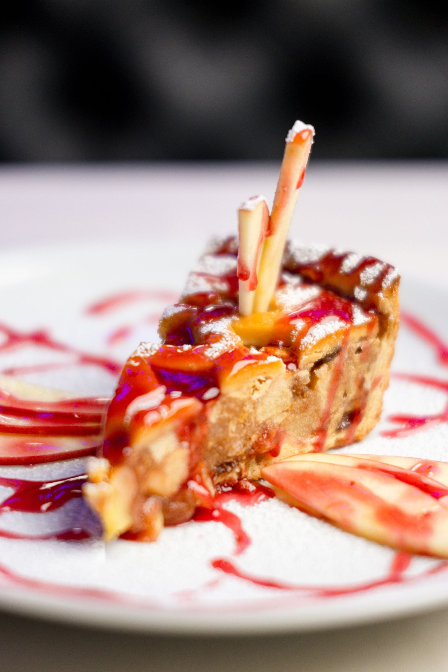 Elegant dessert with caramel sauce and decorative stick garnish plated on white dish with red sauce design.