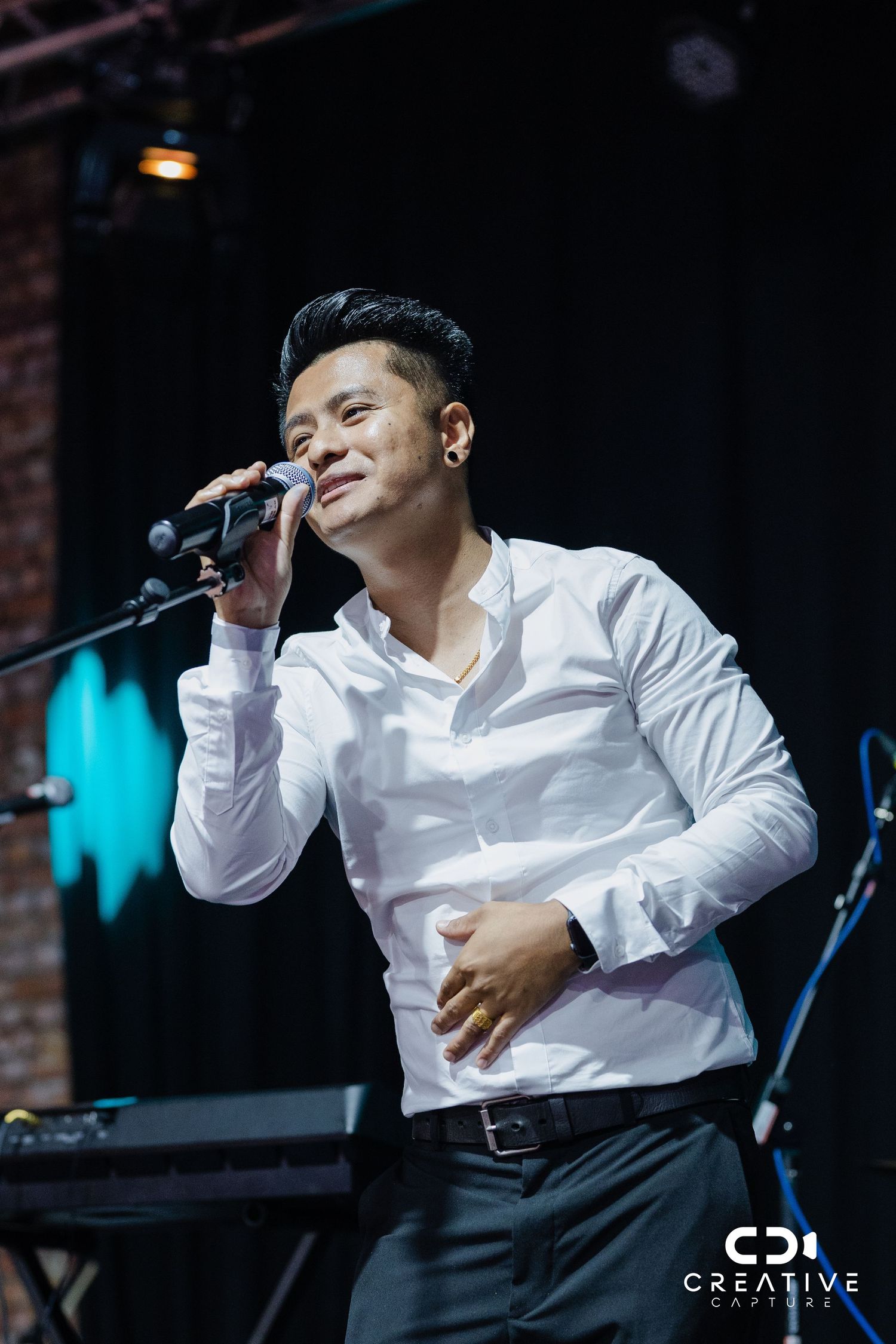 Singer in white dress shirt performing emotively with microphone on stage.