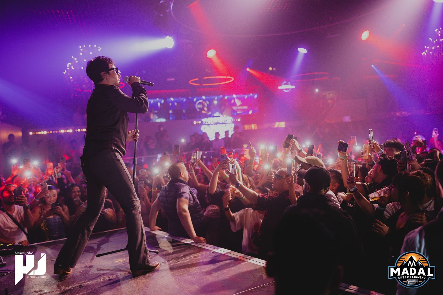 Energetic concert performance with purple lighting and crowd of fans cheering in foreground.