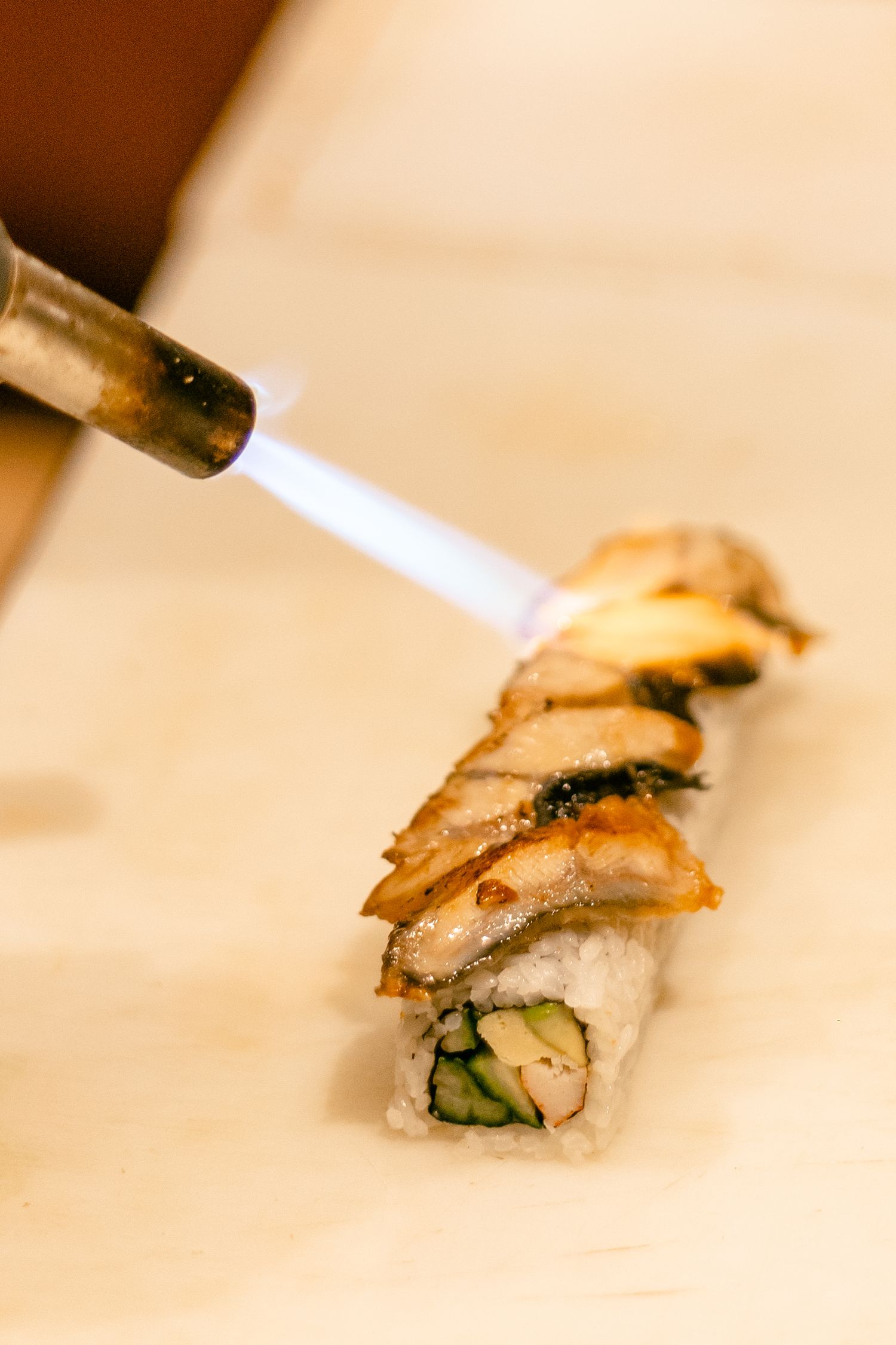 Close-up of sushi being sliced with a knife on a wooden cutting board.