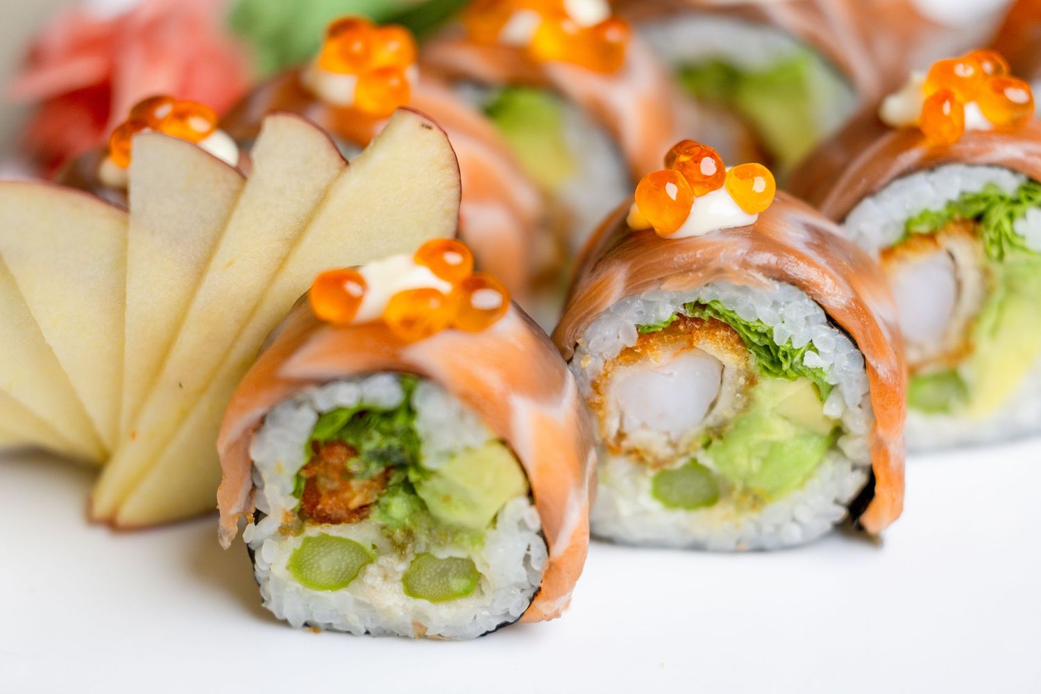 Colorful sushi rolls with salmon, avocado and tobiko arranged in a row on white plate.
