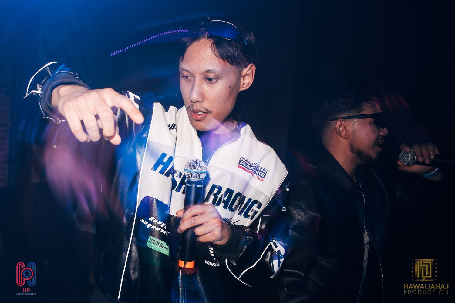 Performer in white jacket singing during nightclub show with blue lighting effects.